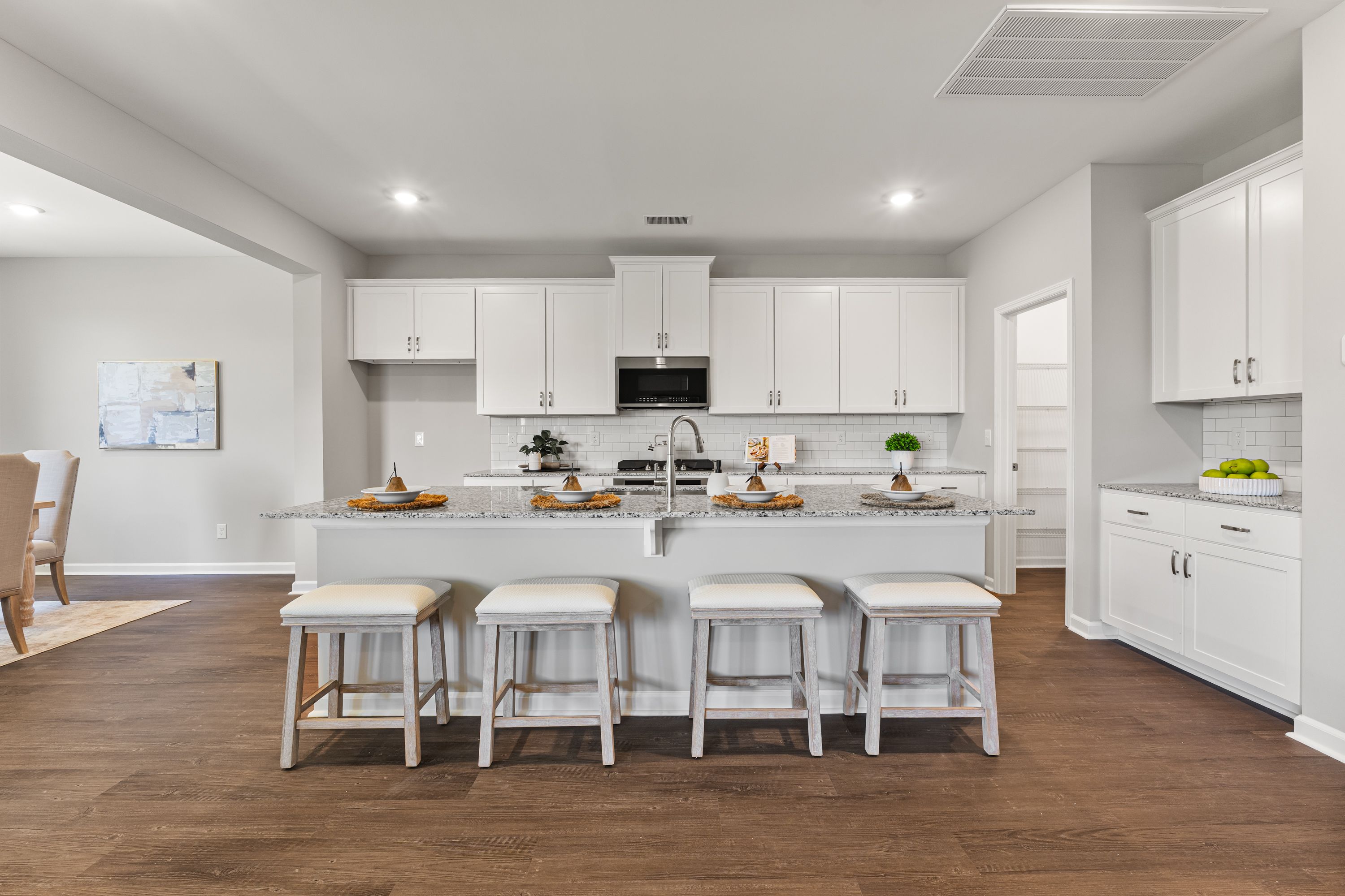 Spacious gourmet kitchen in The Avalon E featuring white shaker cabinets, large island with bar stools, farmhouse sink, and hardwood floors