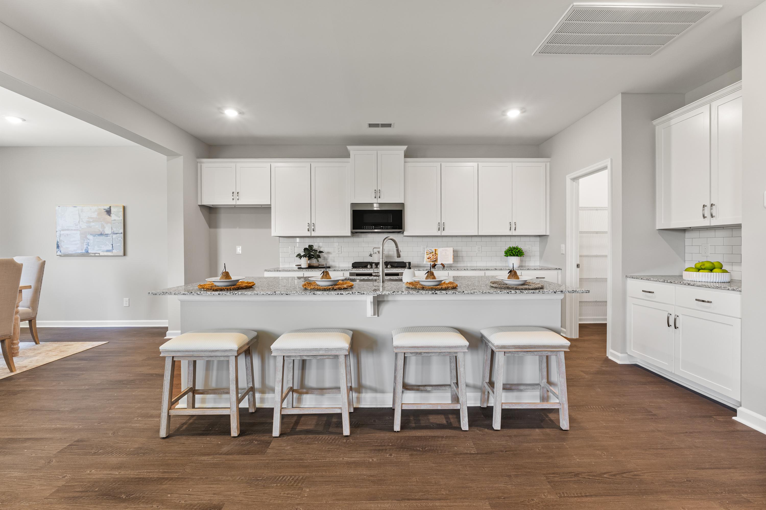 Spacious white kitchen in The Avalon D featuring large island with bar stools, stainless appliances, and open dining area