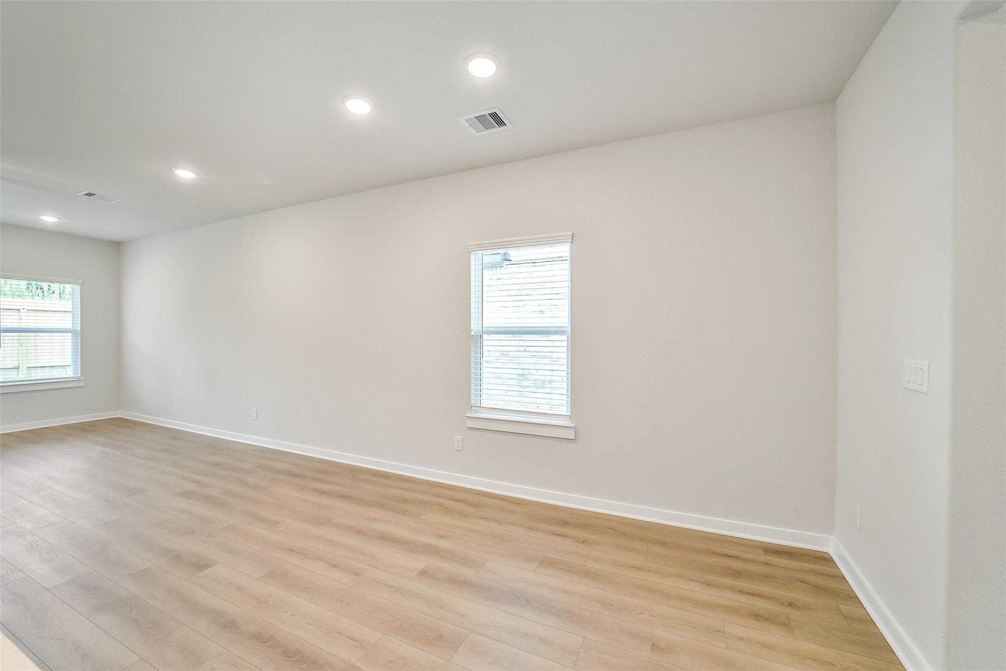 Spacious empty living room with light oak laminate floors, recessed lighting, and large windows in Davidson Homes The Blanco E, Magnolia, Texas
