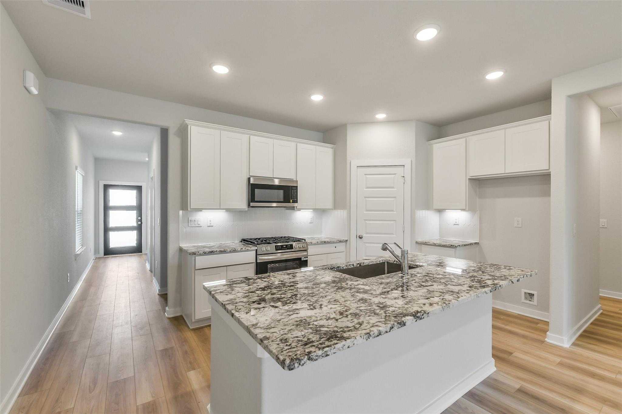 Modern white kitchen with granite island, stainless appliances, open layout in 5-bed Davidson Homes Rio Grande H, Magnolia TX