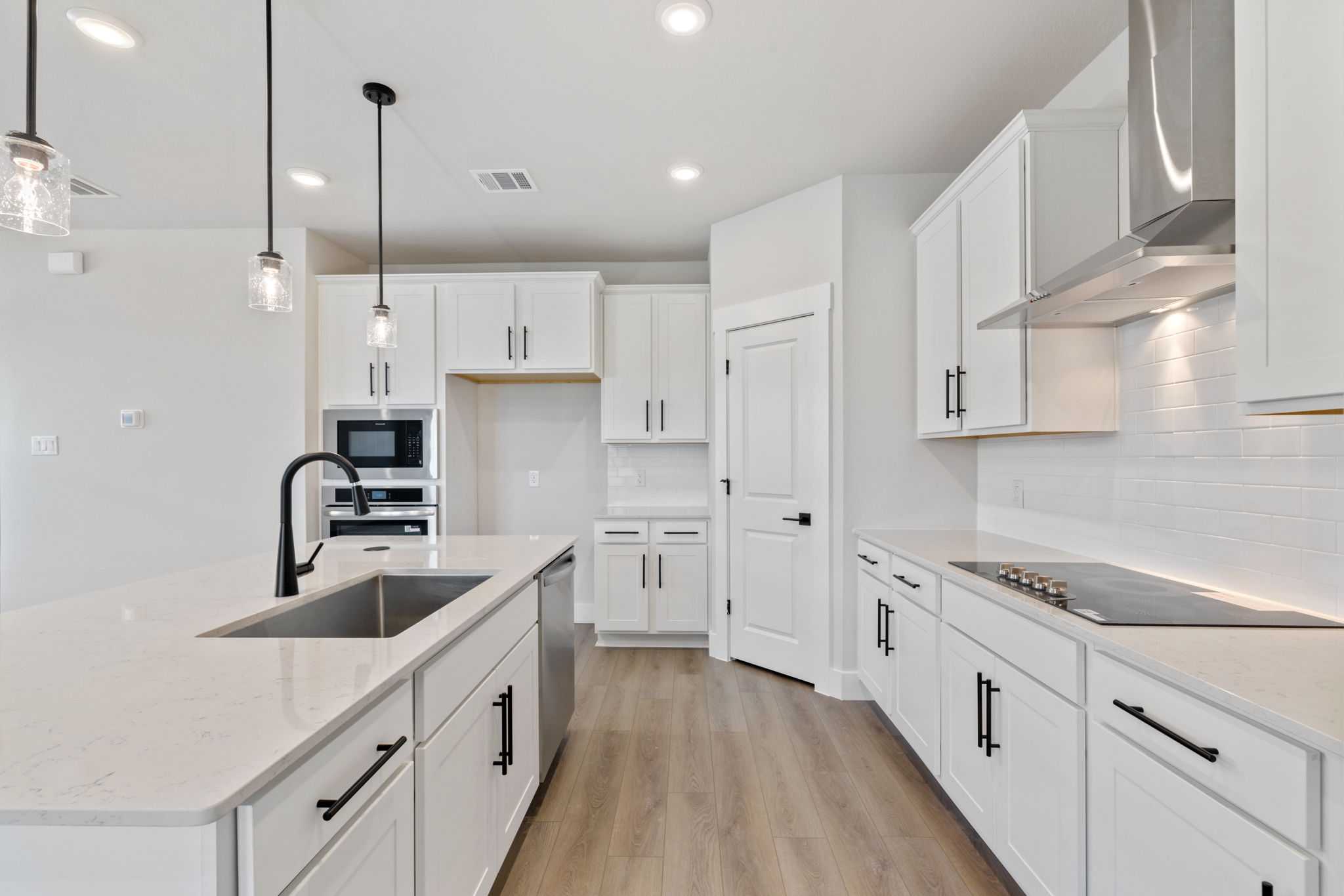Modern white kitchen with quartz island, stainless steel appliances, subway tile backsplash in Davidson Homes The Durham C, Wylie, TX