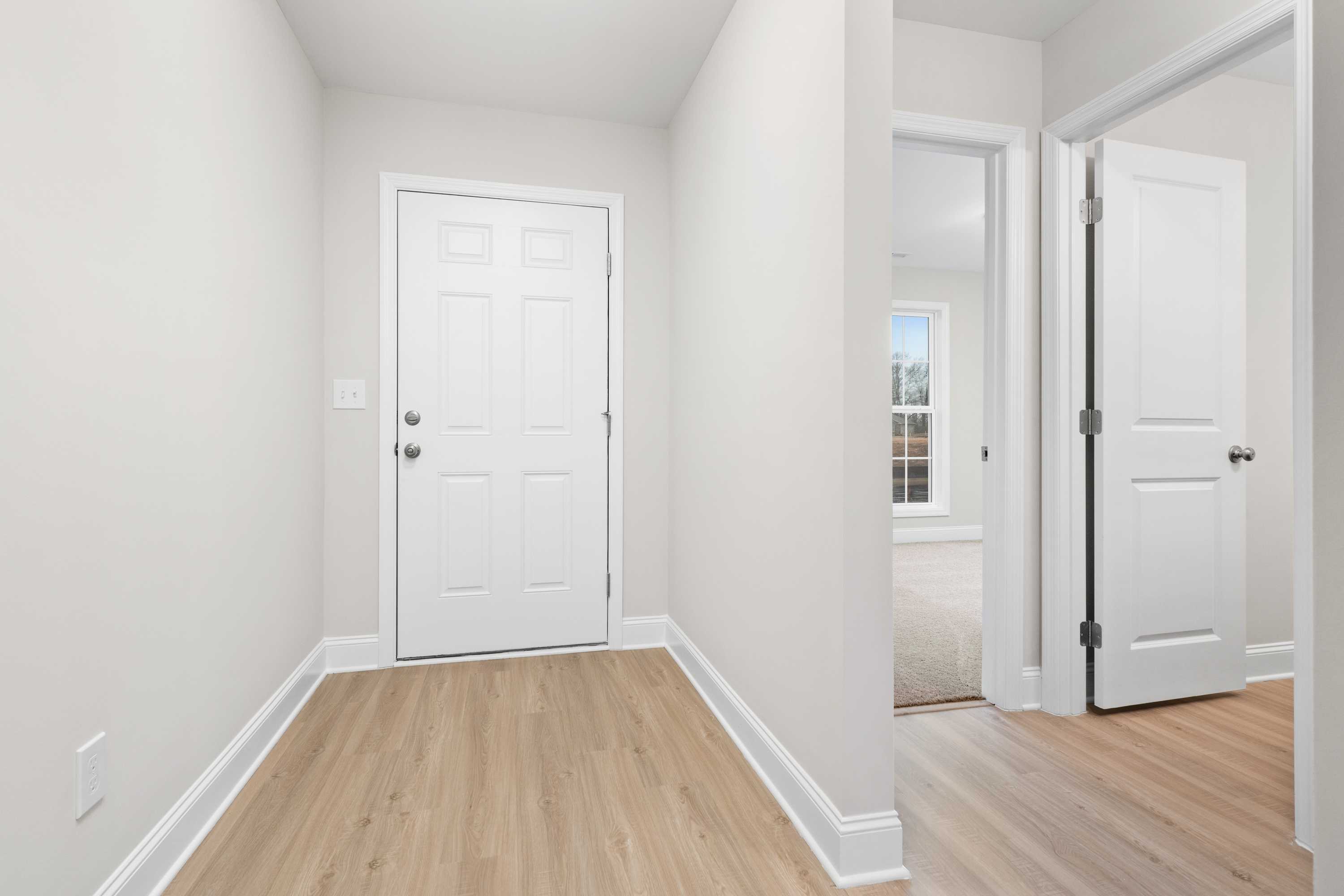 Spacious entryway in The Asheville home design with white paneled doors, light wood flooring, and open hallway to bedroom