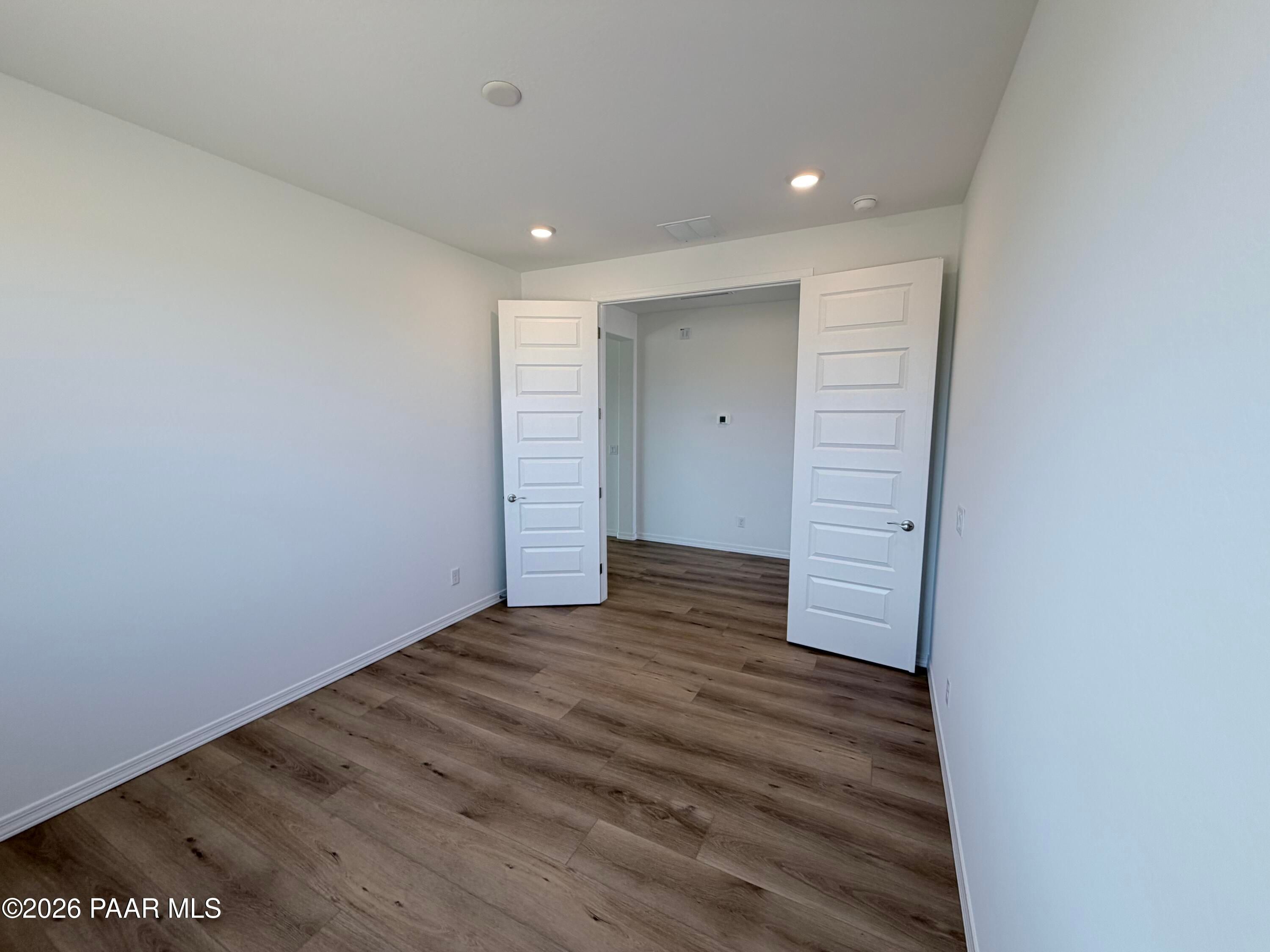 Bright, empty bedroom with wood-look flooring and double doors in The Inspiration C floor plan at Pronghorn Ranch.