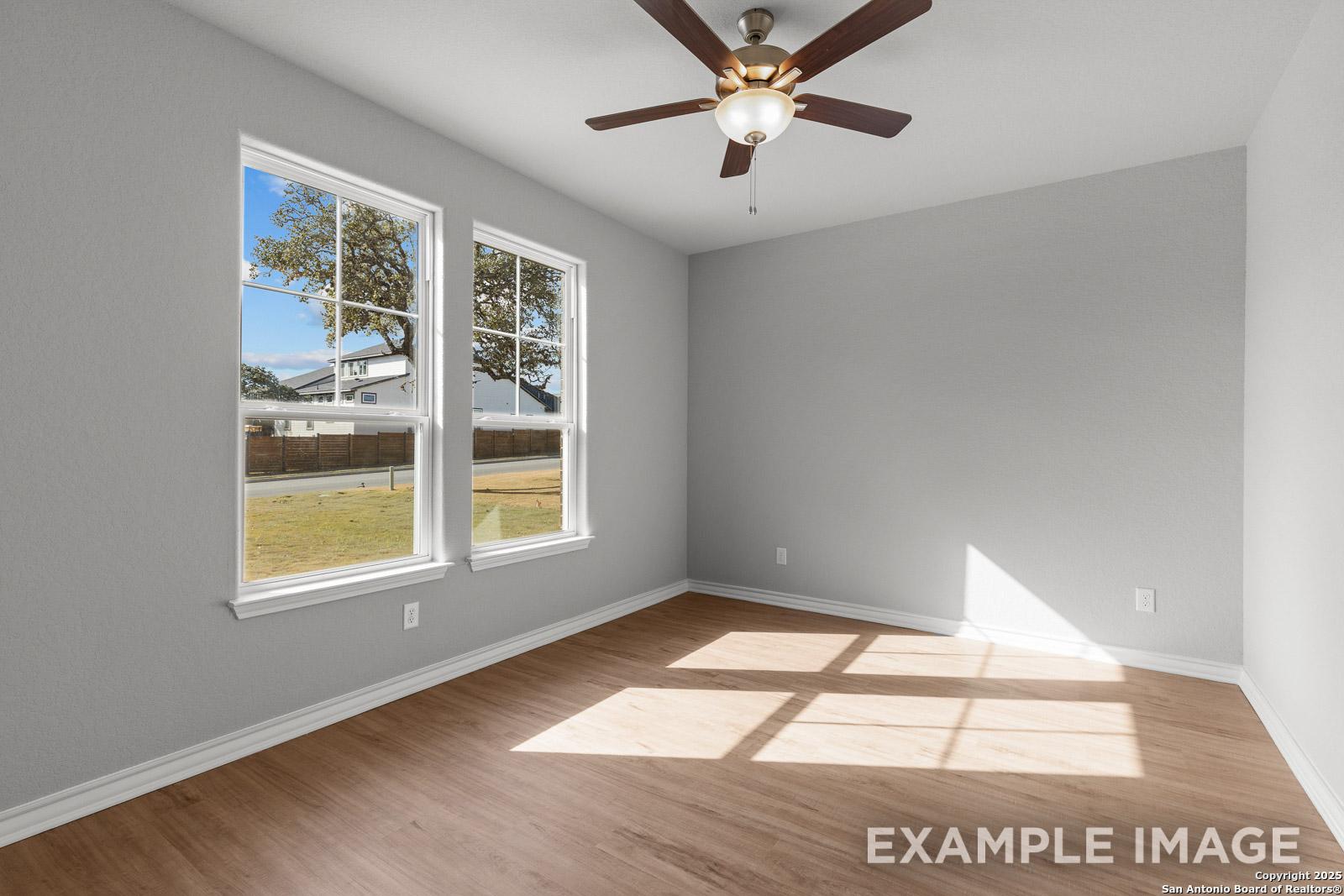 Bright bedroom in The Oxford H floor plan featuring wood-look flooring, neutral grey walls, and a ceiling fan.