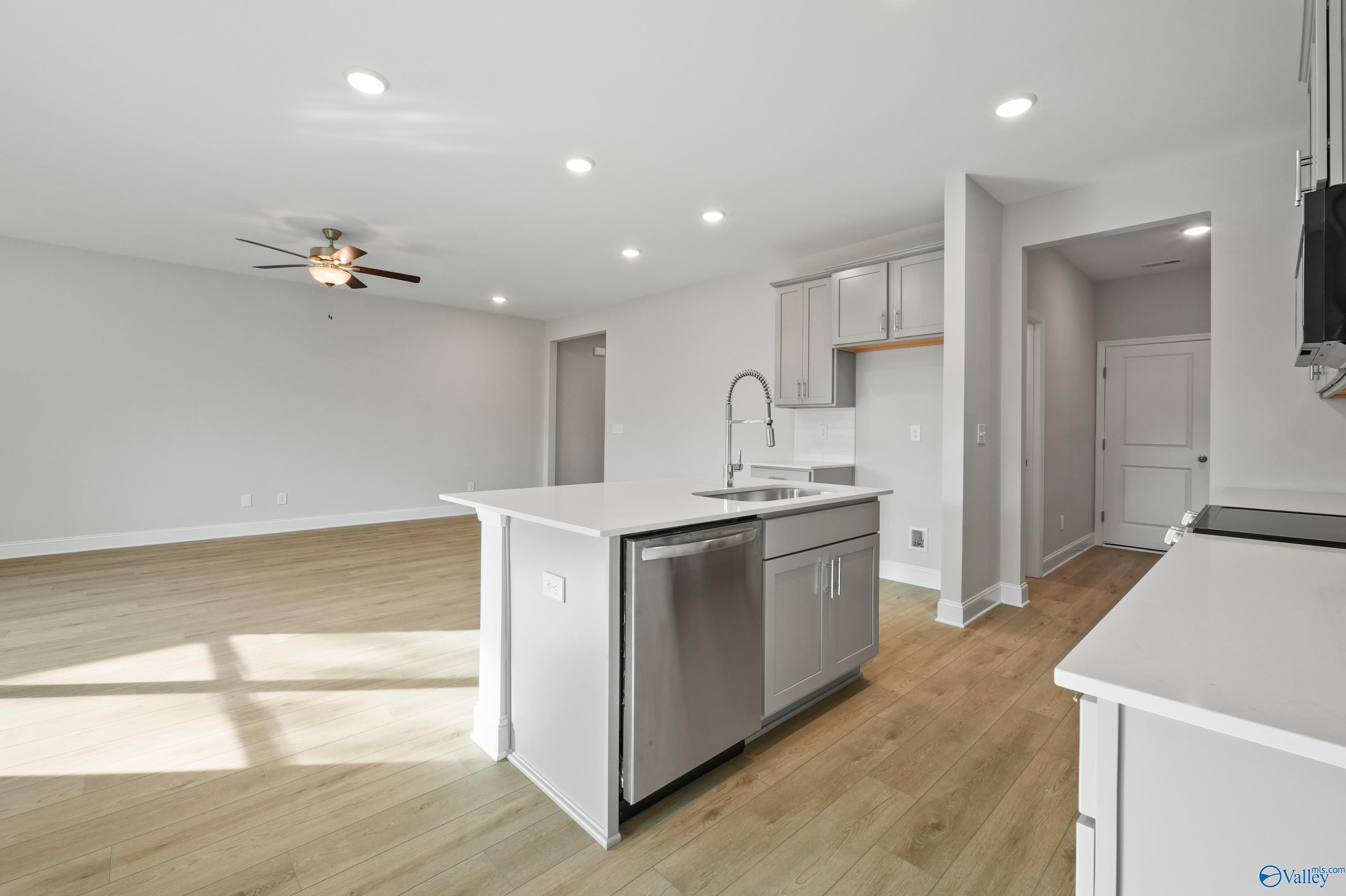 Modern open-concept kitchen with white island sink, stainless dishwasher, and hardwood floors in The Camden B, Huntsville, AL