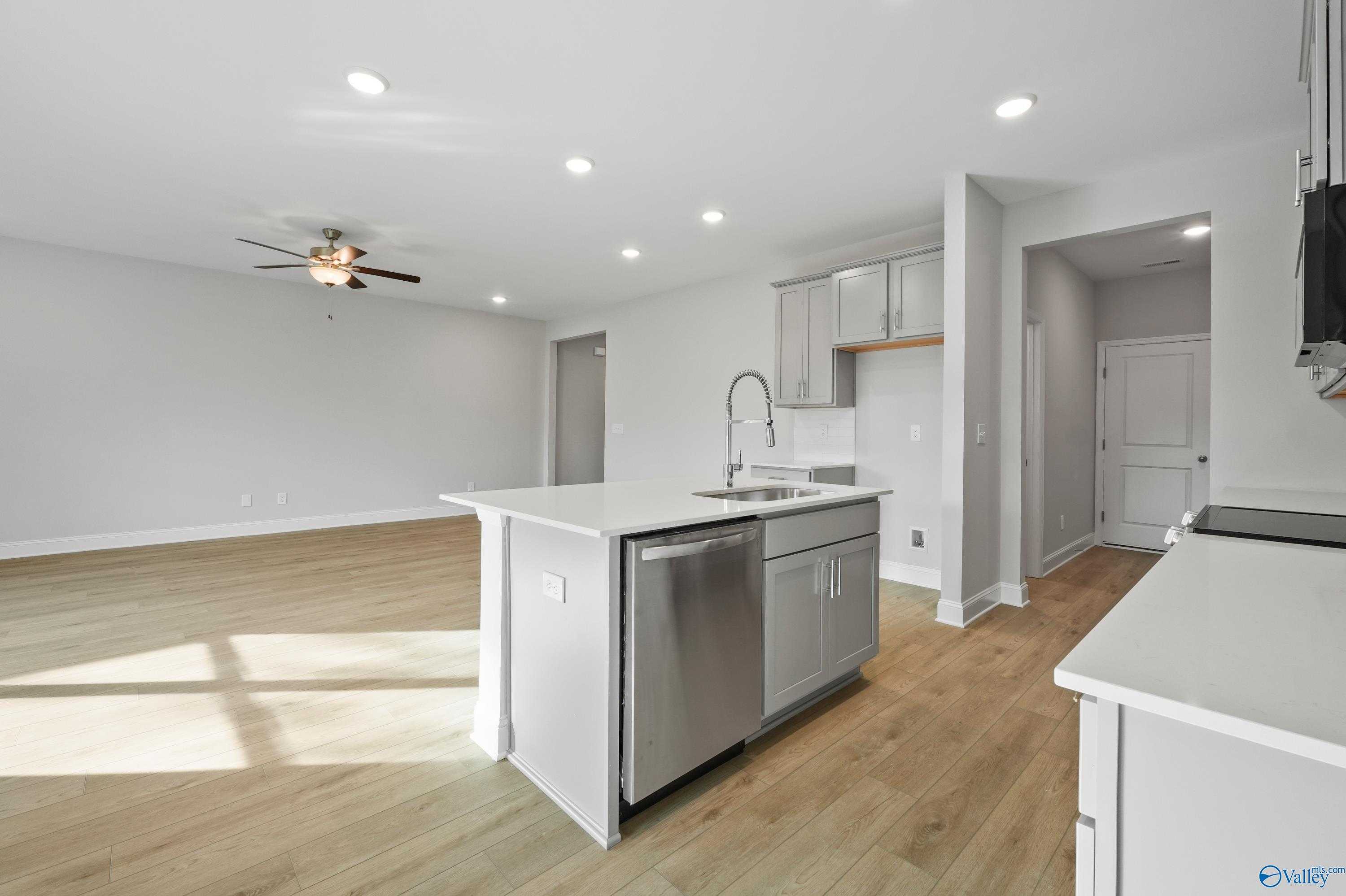 Modern open-concept kitchen with white island sink, stainless dishwasher, and hardwood floors in The Camden B, Huntsville, AL