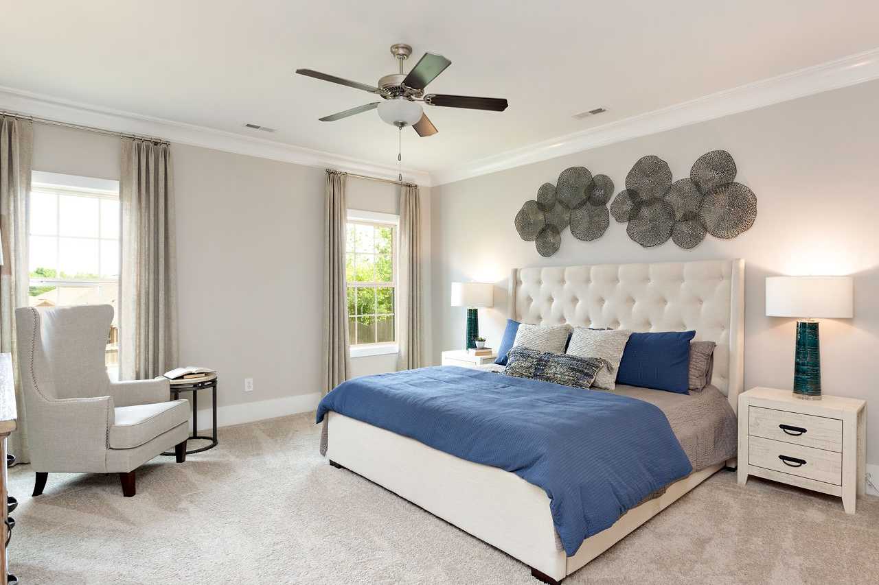 Spacious master bedroom at Laurenwood Preserve in Madison AL with king bed, tufted headboard, ceiling fans, and neutral decor