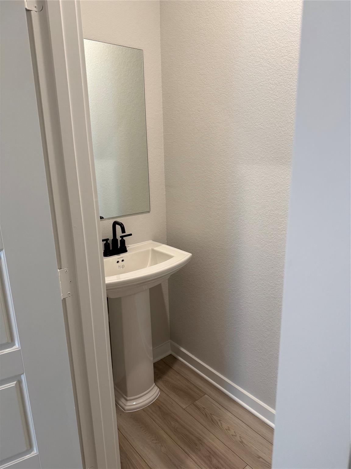 Modern powder room with pedestal sink, matte black faucet, and wall mirror in The Sorrento E at Sundance Cove, Crosby.