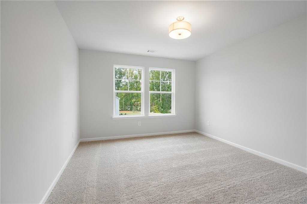 Bright empty bedroom with large windows overlooking trees, carpeted floor in Davidson Homes The Cary A, Kennesaw, Georgia