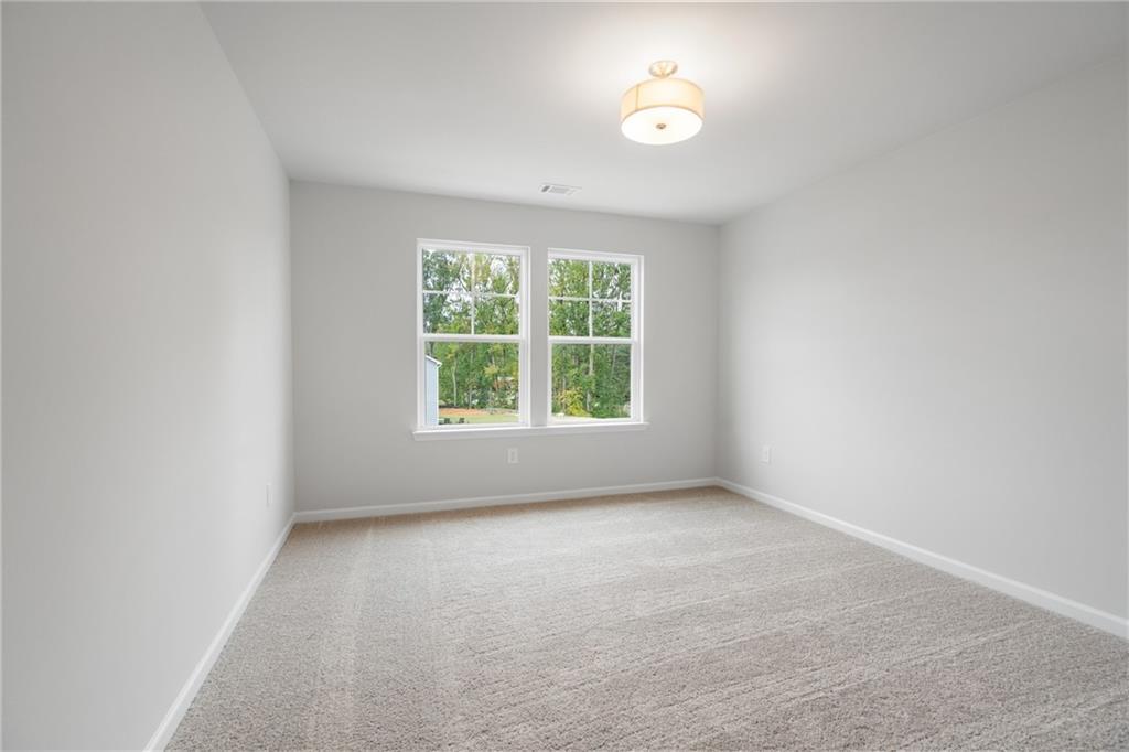 Bright empty bedroom with large windows overlooking trees, beige carpet, ceiling light in Davidson Homes The Cary A, Kennesaw, GA