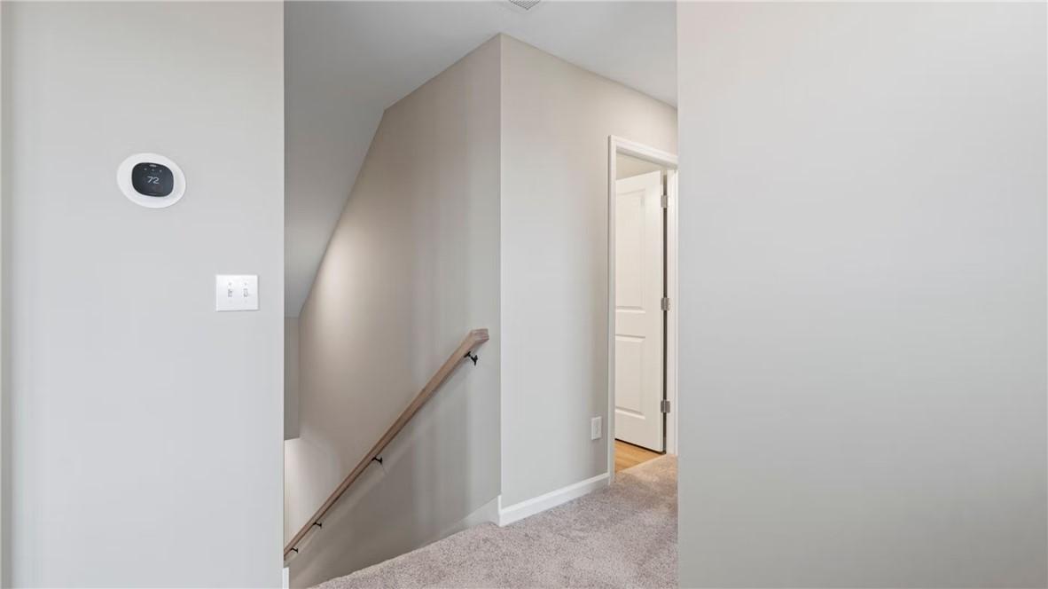 Carpeted staircase with wooden handrail and beige walls in upstairs hallway of The Stella D 4-bedroom home, Cusseta, Alabama
