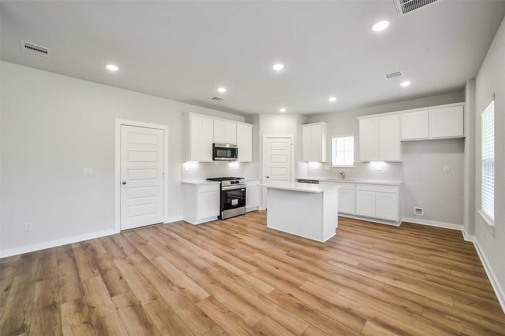 Modern open kitchen with white cabinetry, center island, stainless steel oven and microwave in Davidson Homes The Trinity F, Magnolia TX