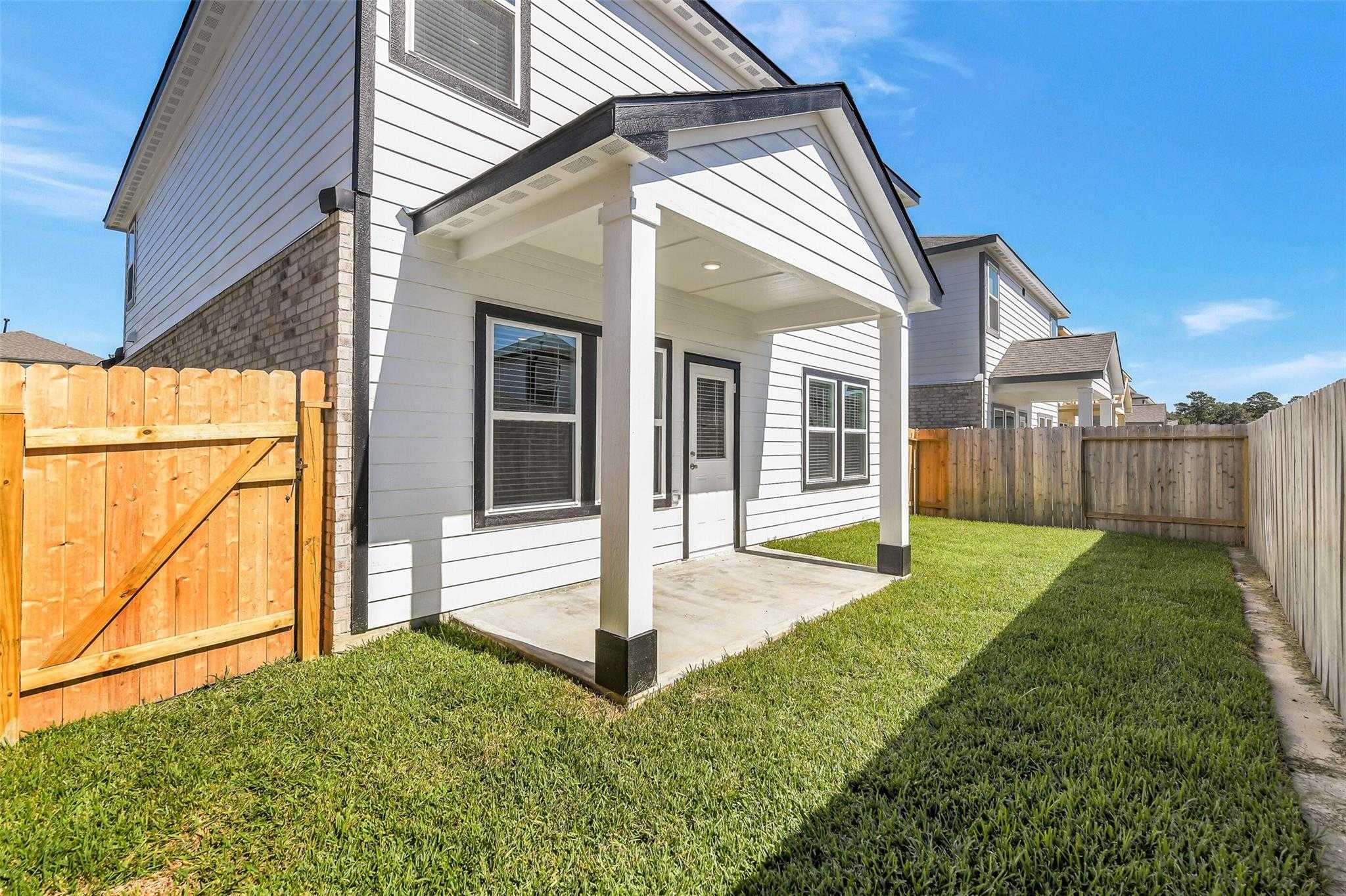 Covered back patio with white columns, large windows, and fenced grassy yard in Davidson Homes The Rio Grande H, Magnolia, Texas