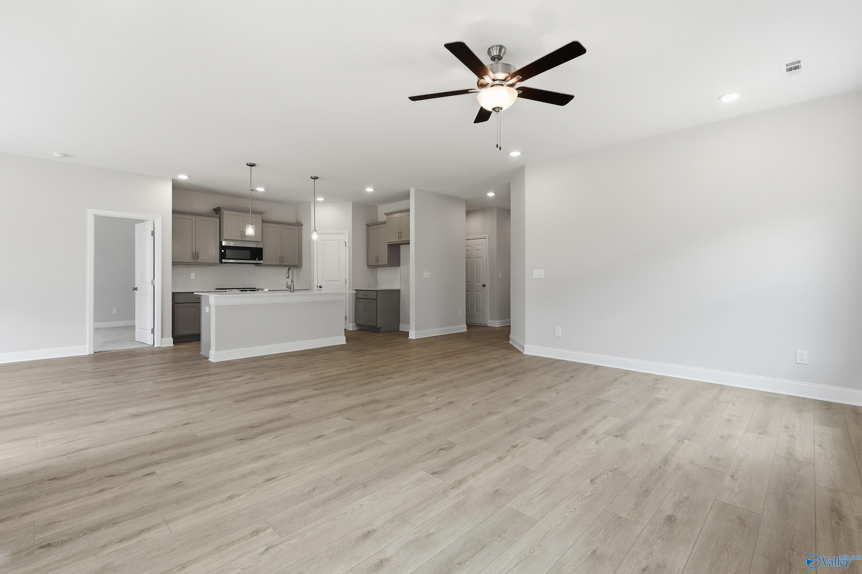 Open kitchen and living area with gray cabinets, large island, dual ceiling fans, and light hardwood floors in Davidson Homes The Franklin, Meridianville, AL