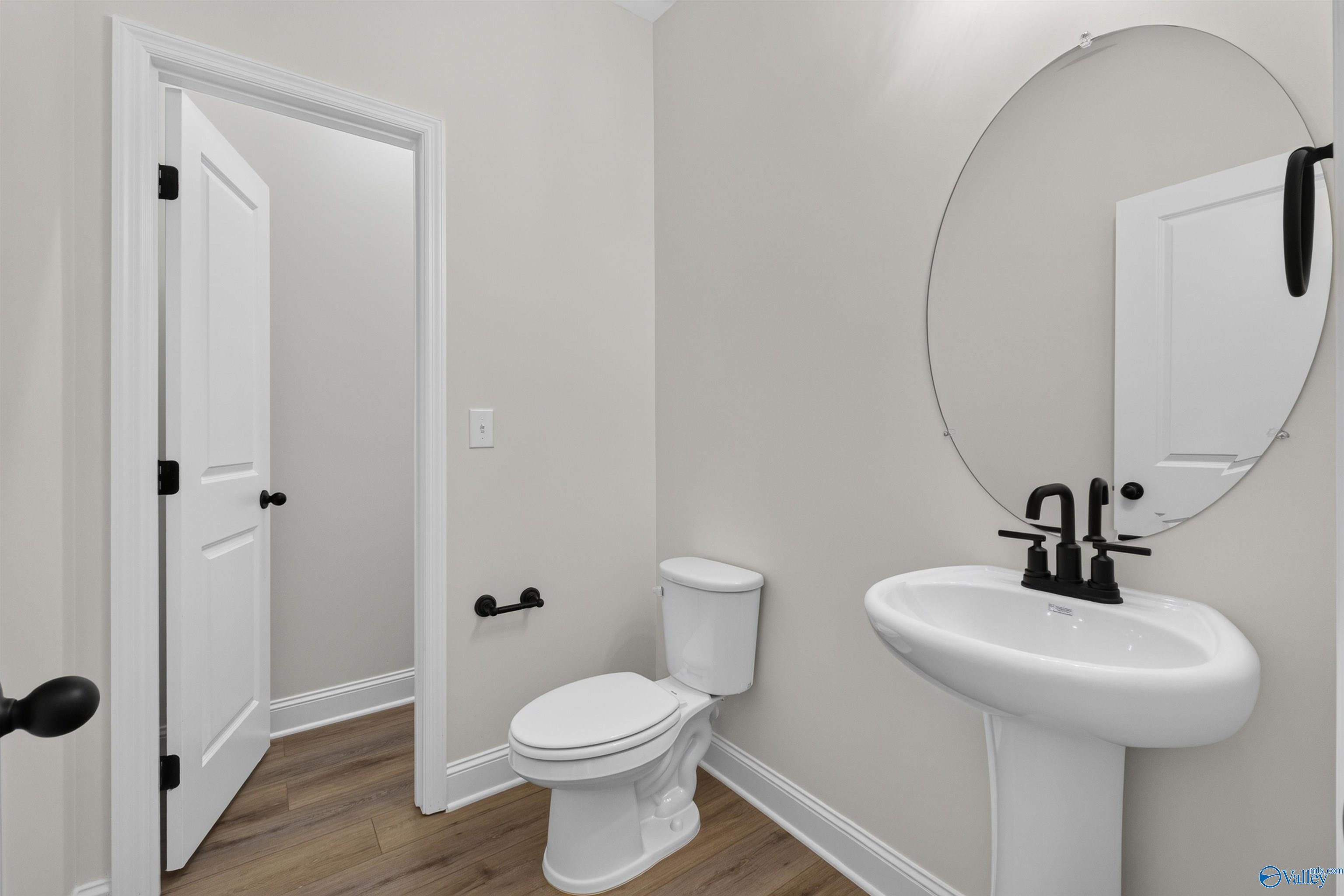 Powder room with pedestal sink, black matte faucet, round mirror, and white toilet in Davidson Homes Ashport L, New Market, AL