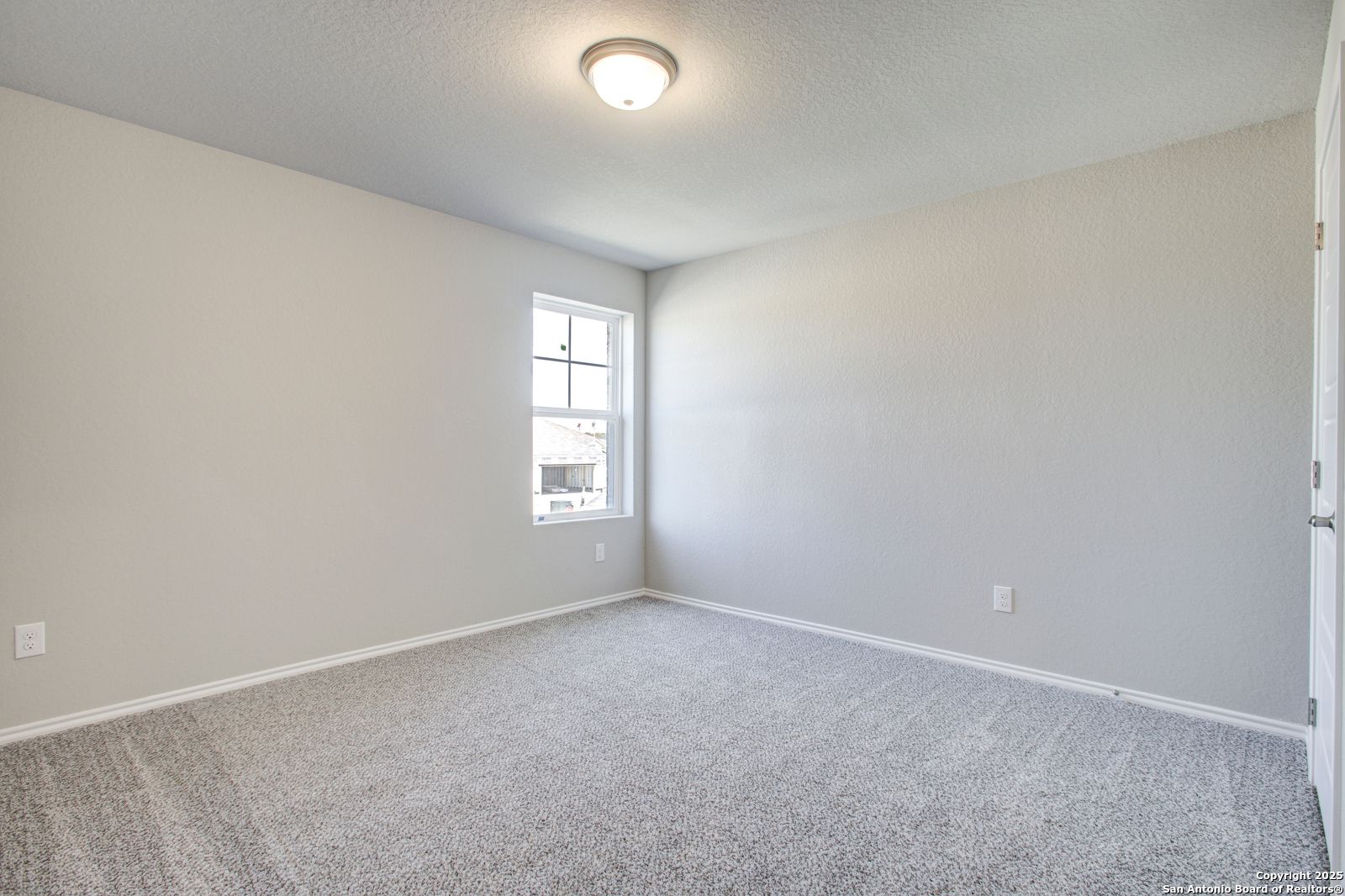 Spacious empty bedroom with beige walls, gray carpet, large window, and ceiling light in Davidson Homes The Douglas G, San Antonio