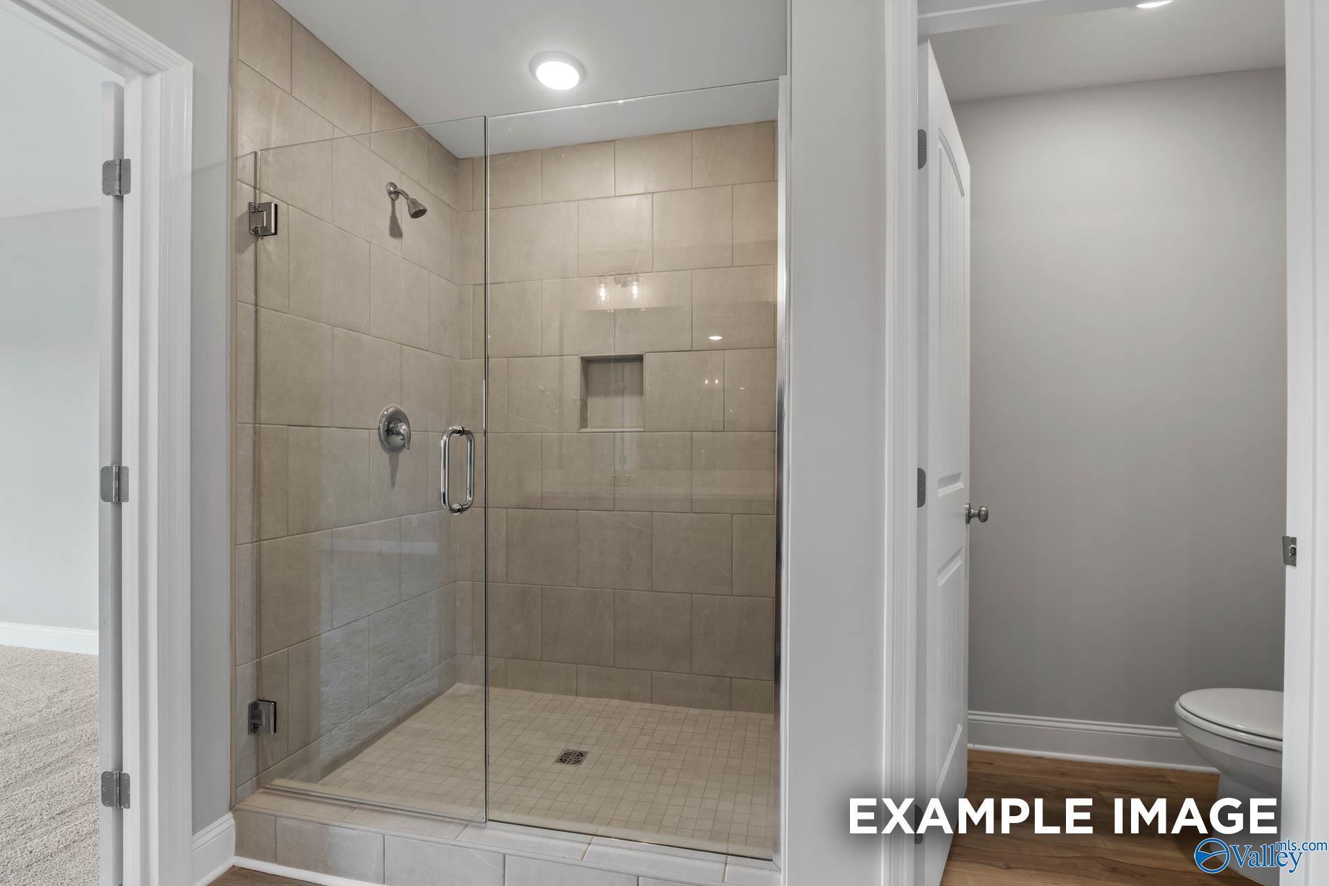 Modern frameless glass shower with beige tile and niche in master bath of The Shelby B by Davidson Homes, New Market, AL