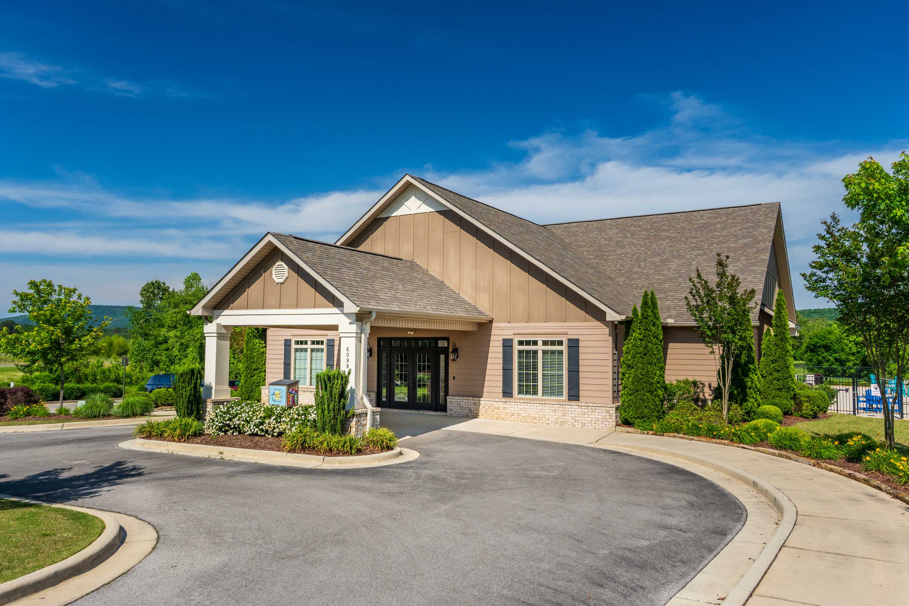 Clubhouse exterior at The Meadows at Hampton Cove in Owens Cross Roads AL featuring covered entrance, landscaped grounds, and adjacent swimming pool