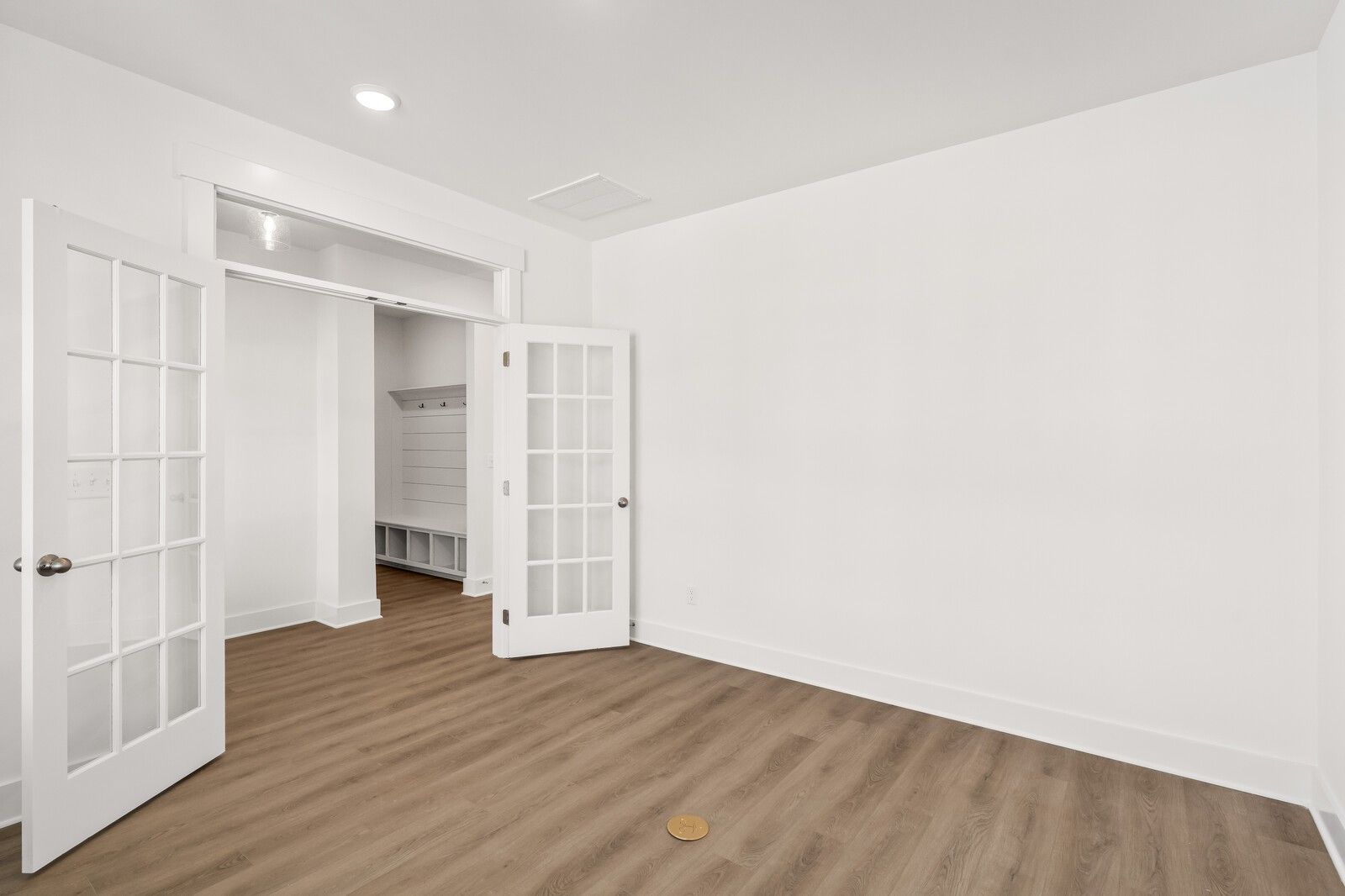 Spacious mudroom with open white French doors, built-in benches, and hardwood floors in Davidson Homes The Ash A, Gallatin, TN