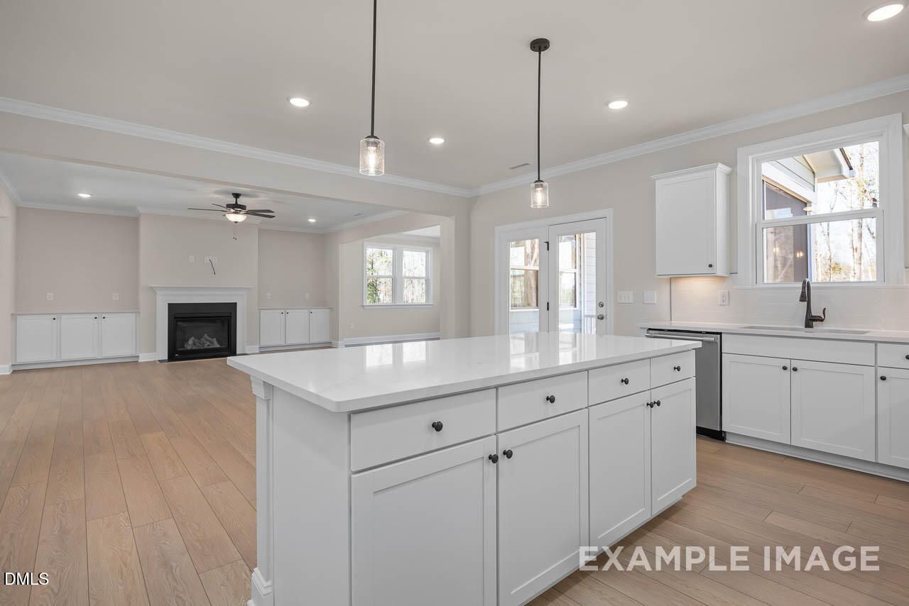 Open-concept kitchen and living room with white shaker cabinets, large island, gas fireplace, hardwood floors in Davidson Homes The Crawford D, Angier, NC