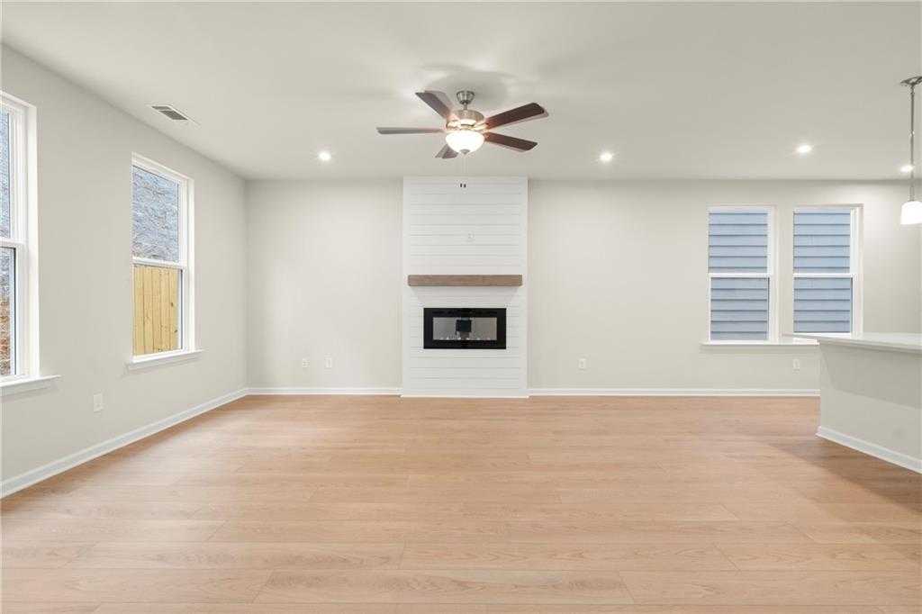 Bright living room with white shiplap fireplace, hardwood floors, large windows in The Cary A by Davidson Homes, Kennesaw, GA