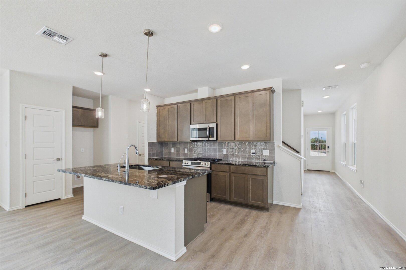 Modern kitchen with granite island and dark wood cabinets in The Charlotte B floor plan at Meadows at Oak Creek, San Antonio.