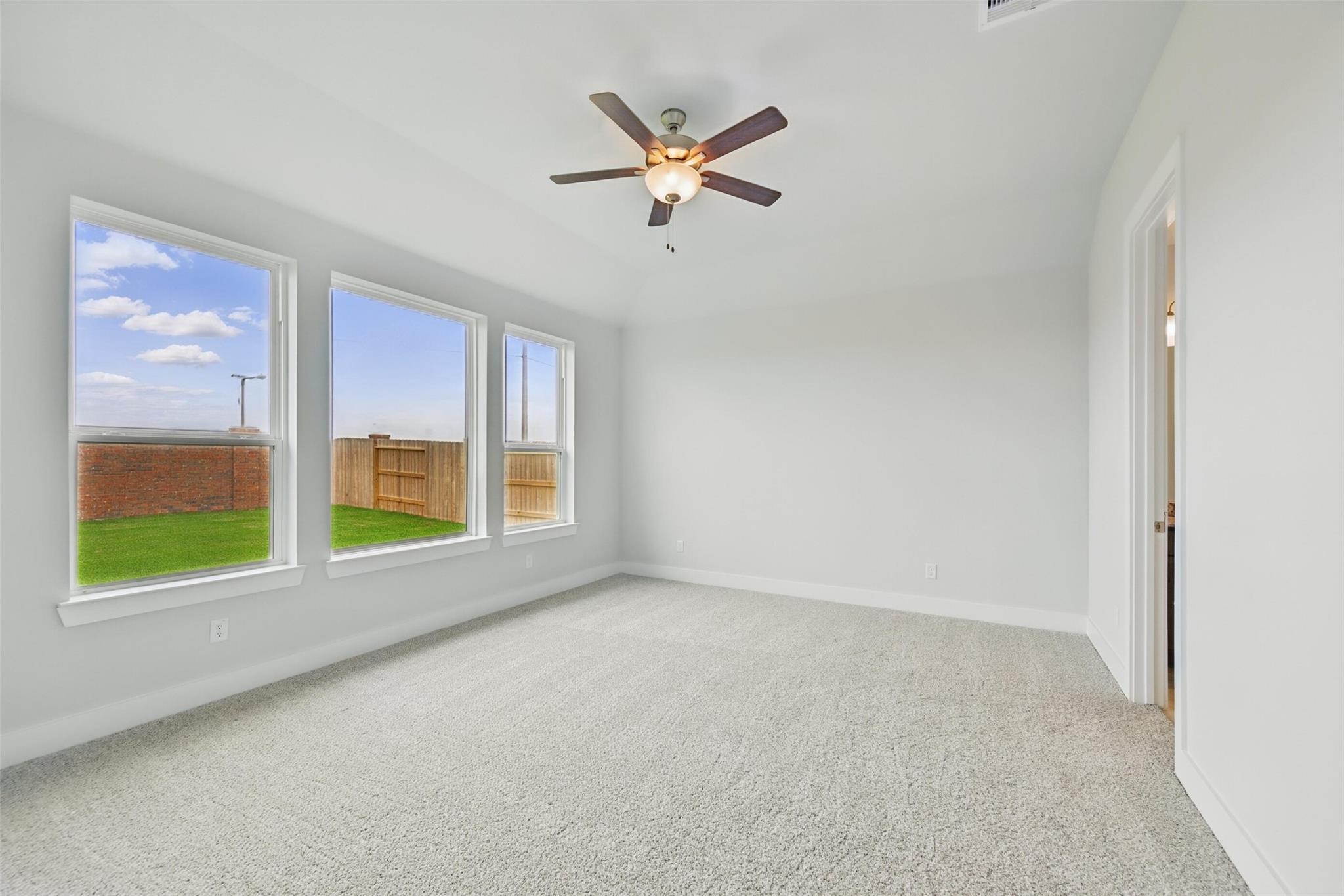 Bright bedroom with large windows, ceiling fan, and backyard view in Davidson Homes The Philip A, Lago Mar, Texas City