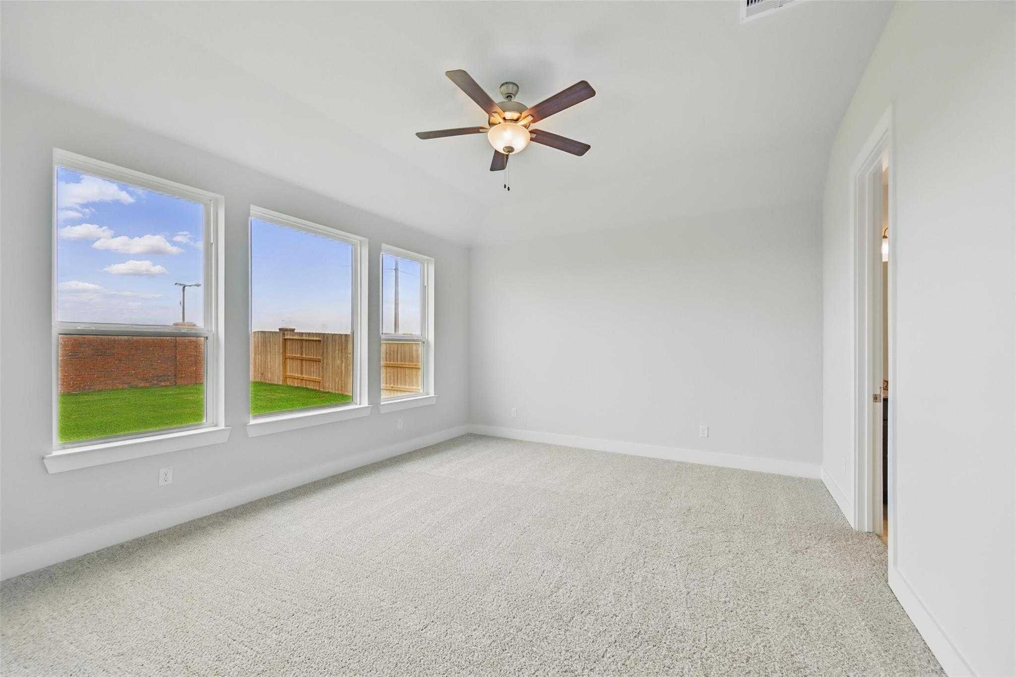 Bright bedroom with large windows, ceiling fan, and backyard view in Davidson Homes The Philip A, Lago Mar, Texas City