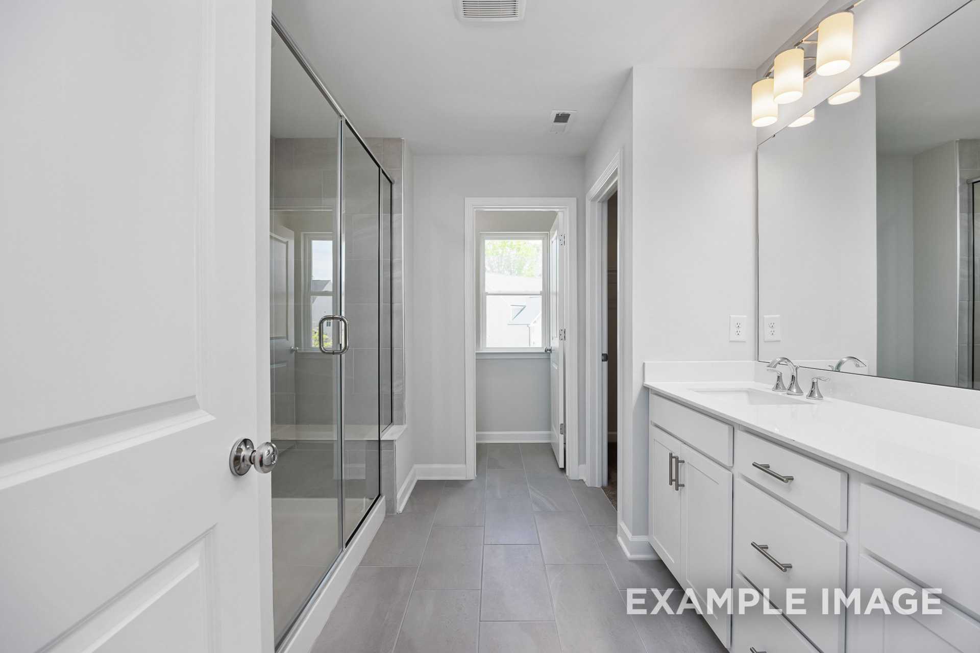 Spacious master bathroom in The Gavin C featuring frameless glass shower, double vanity with white cabinetry, and gray tile flooring
