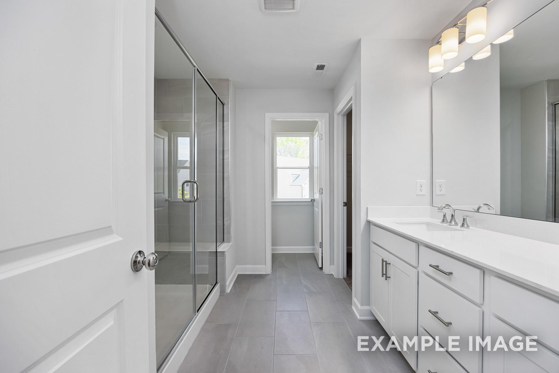 Spacious master bathroom in The Gavin B with frameless glass shower, double white vanity, and modern lighting