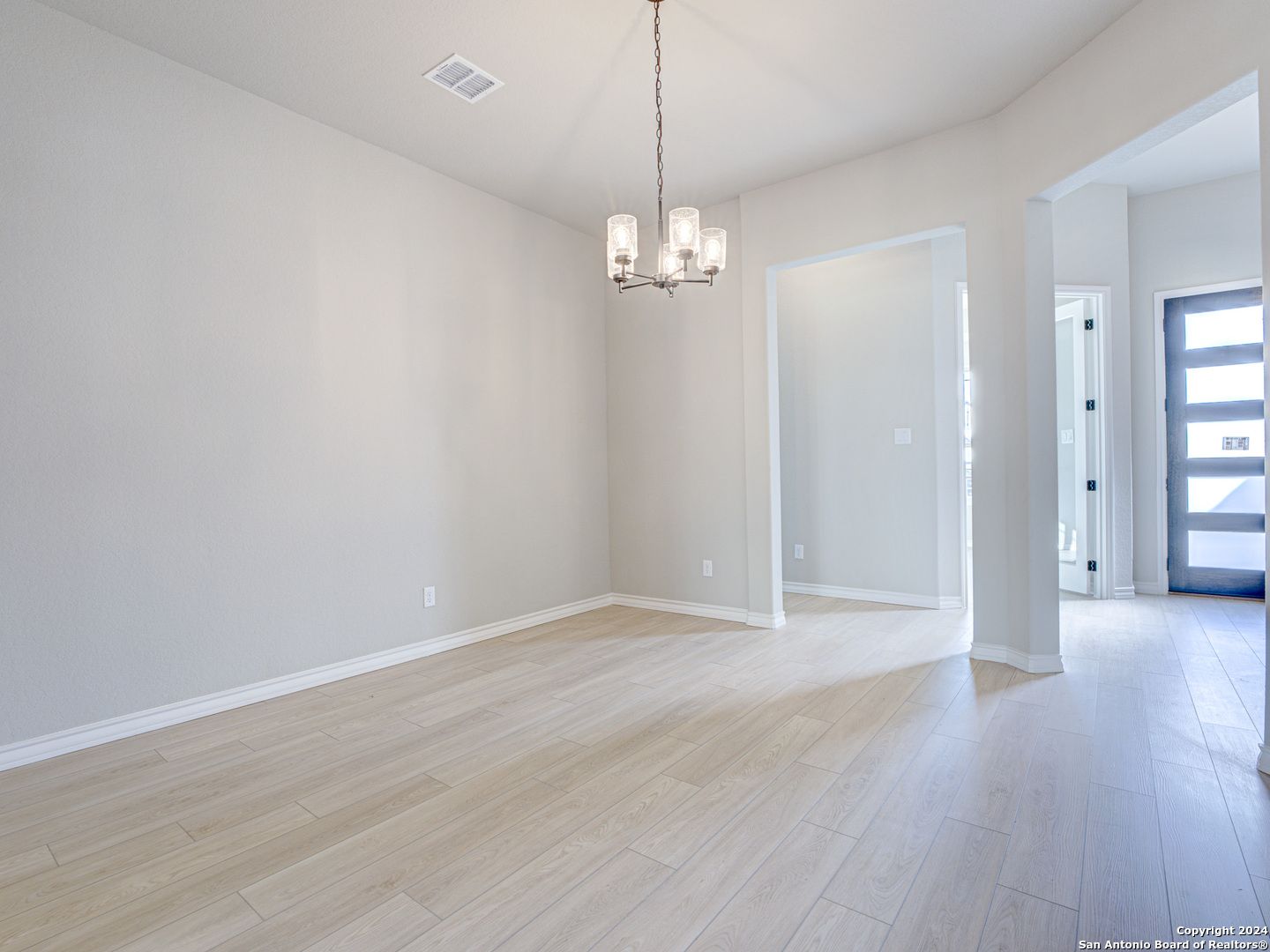 Bright dining room with modern chandelier, light hardwood floors, and open archway in Davidson Homes The Summerlin A, Castroville, Texas