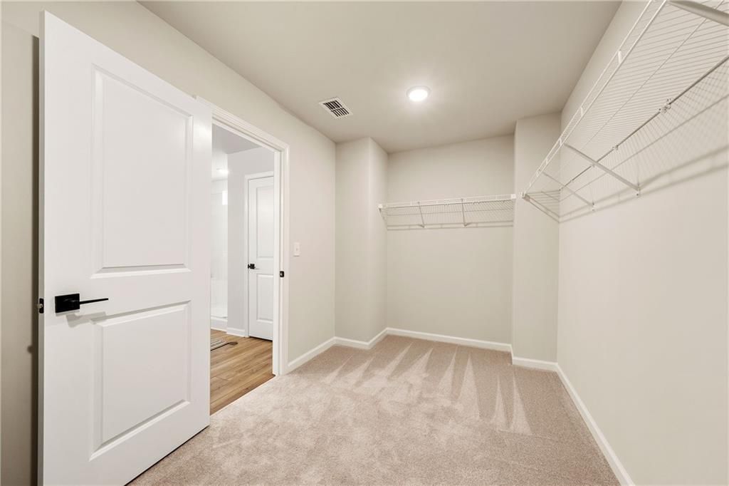 Spacious walk-in closet with wire shelving, white doors, and neutral carpet in Davidson Homes The Willow B, Riverwood, Dallas, Georgia