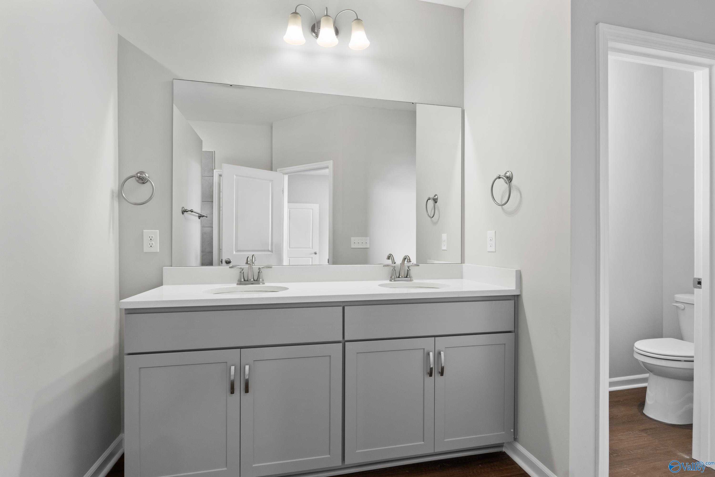 Modern master bathroom with double gray vanity, large mirrors, and vanity lights in Davidson Homes The Dorado, Athens, Alabama