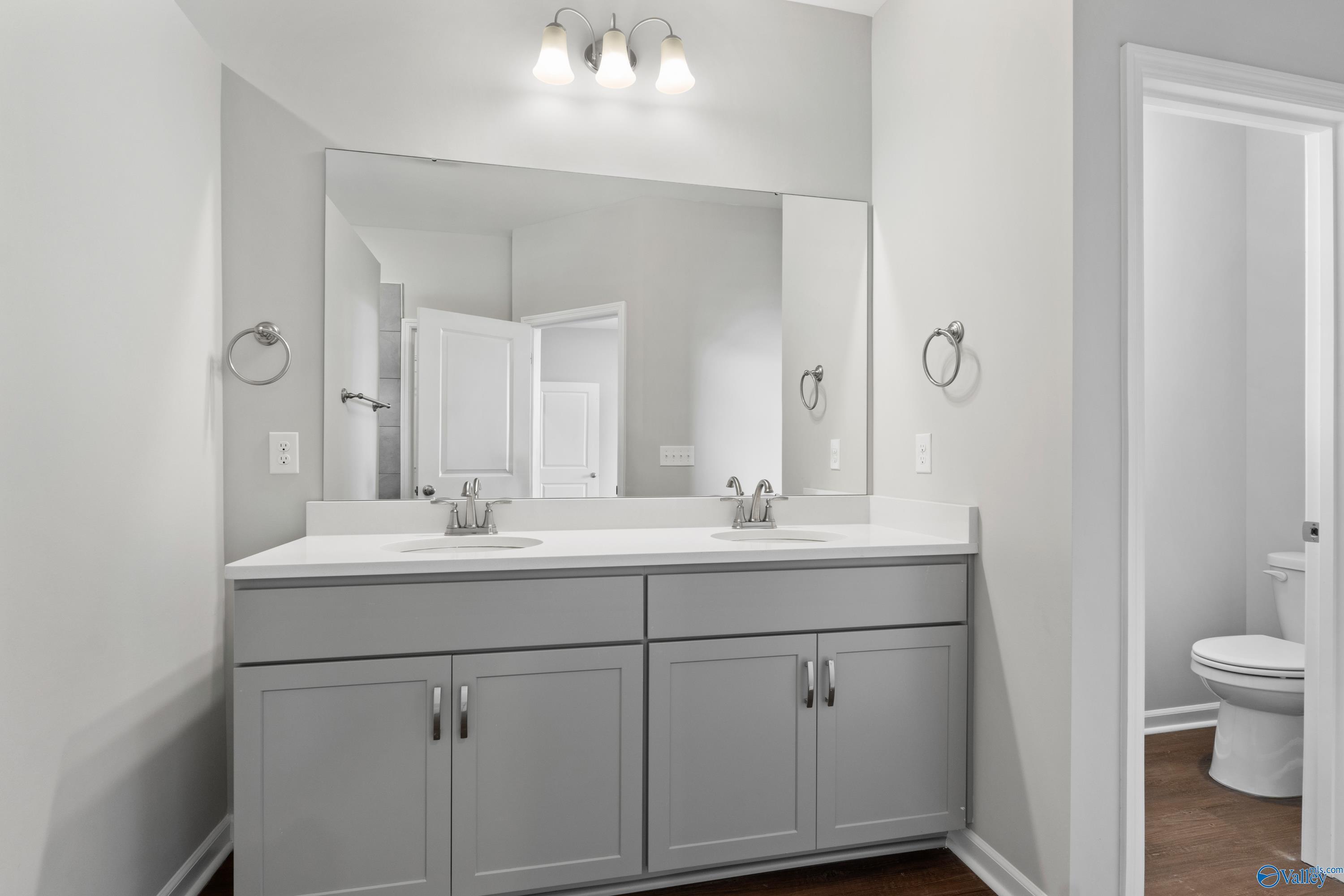 Modern master bathroom featuring double gray vanity, large mirror, and adjacent toilet in Davidson Homes The Dorado, Athens AL