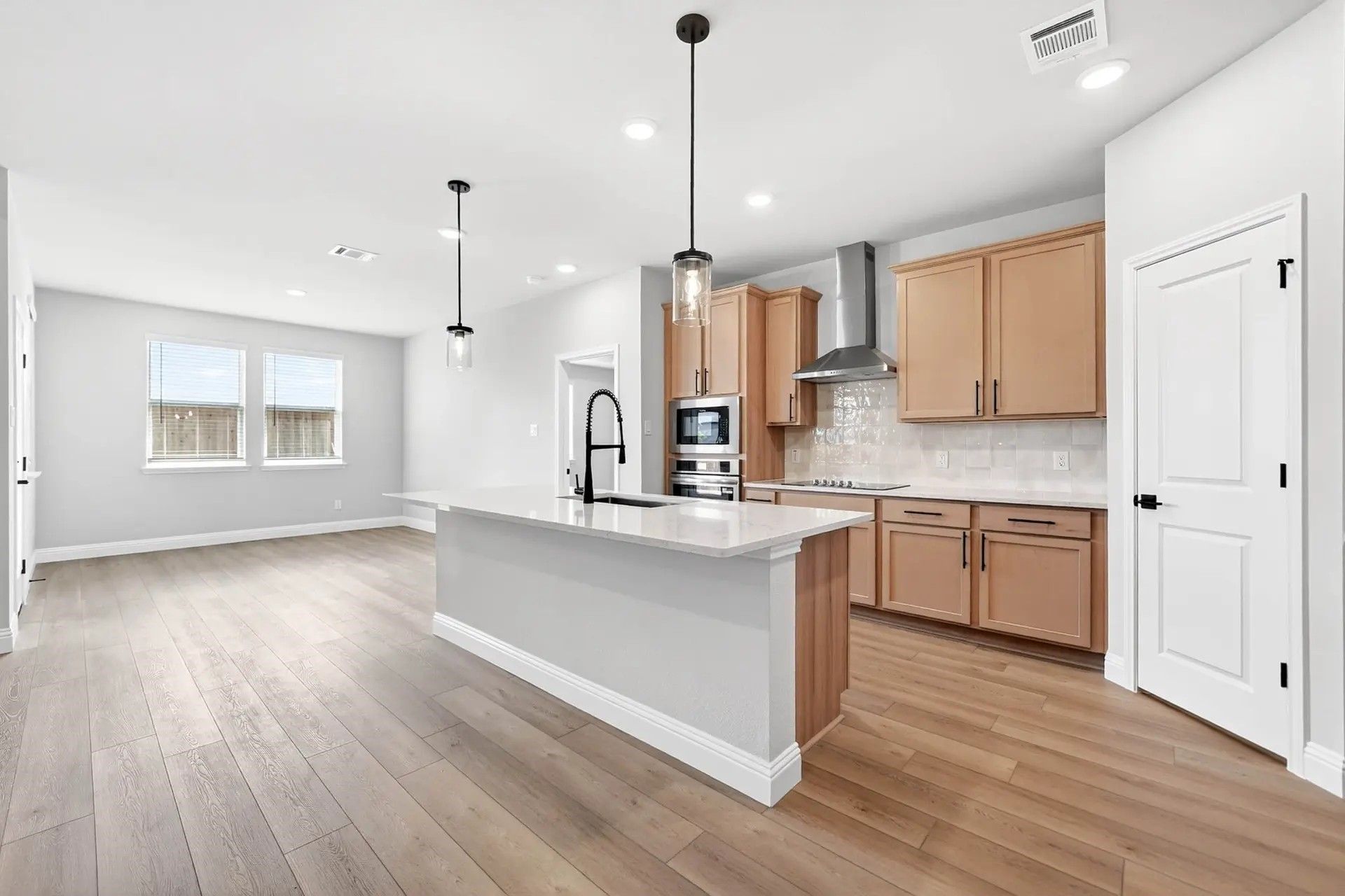 Modern kitchen with light wood cabinets, quartz island, and stainless appliances in The Holly C home in Heartland, Texas.