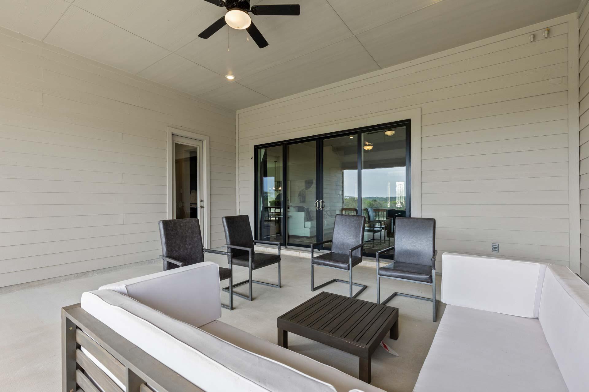 Covered patio with white sectional sofa, chairs, and ceiling fan at Potranco Oaks in Castroville Texas by Davidson Homes