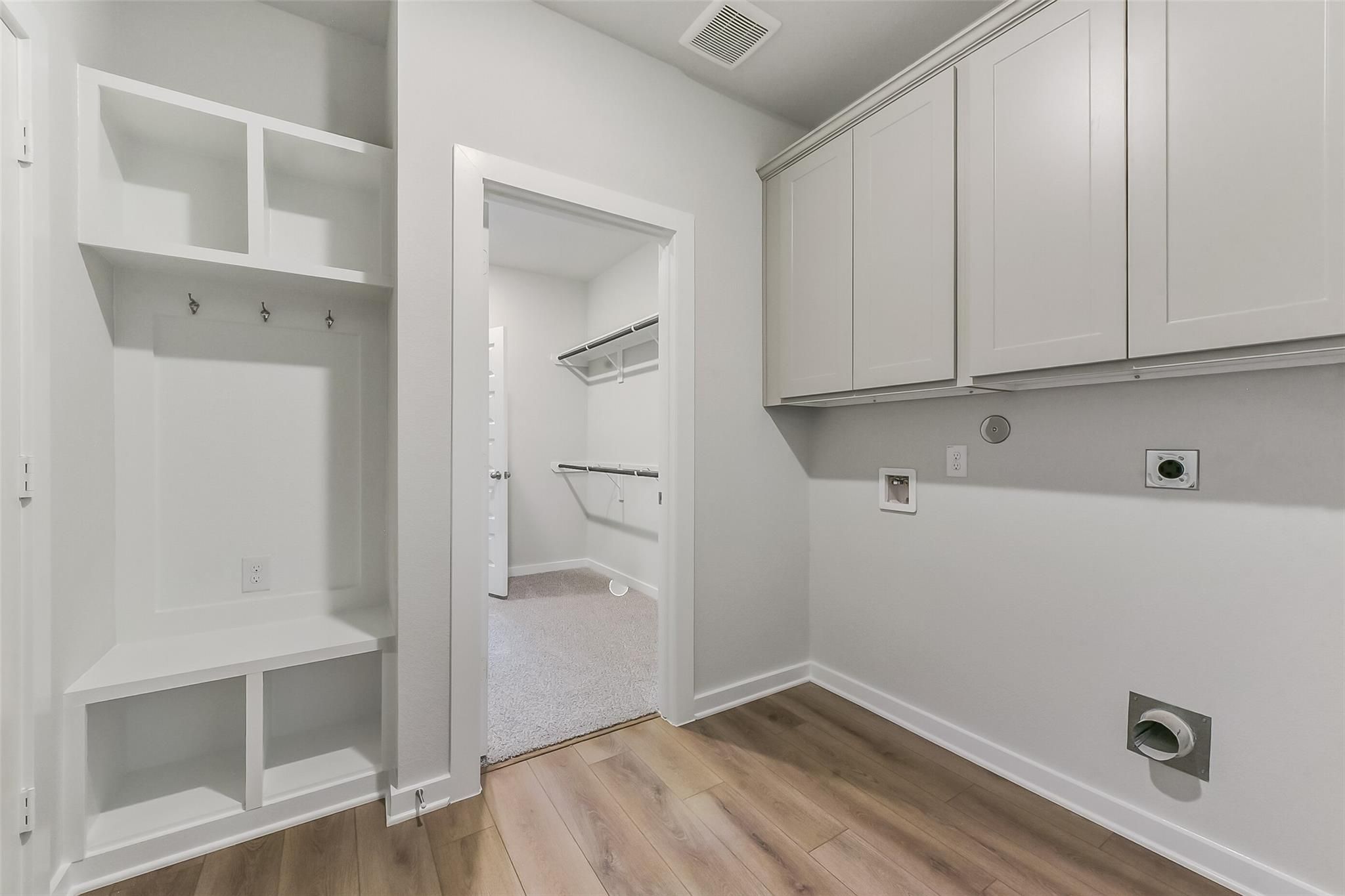 Modern laundry room with white shaker cabinets, built-in bench, coat hooks in Davidson Homes The Tierra C, Dayton, Texas