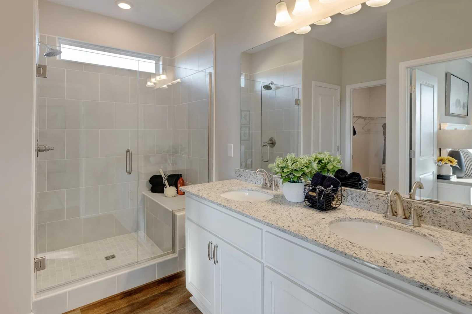 Spacious master bathroom in The Aurora B featuring double quartz vanity, frameless glass shower, and neutral tones