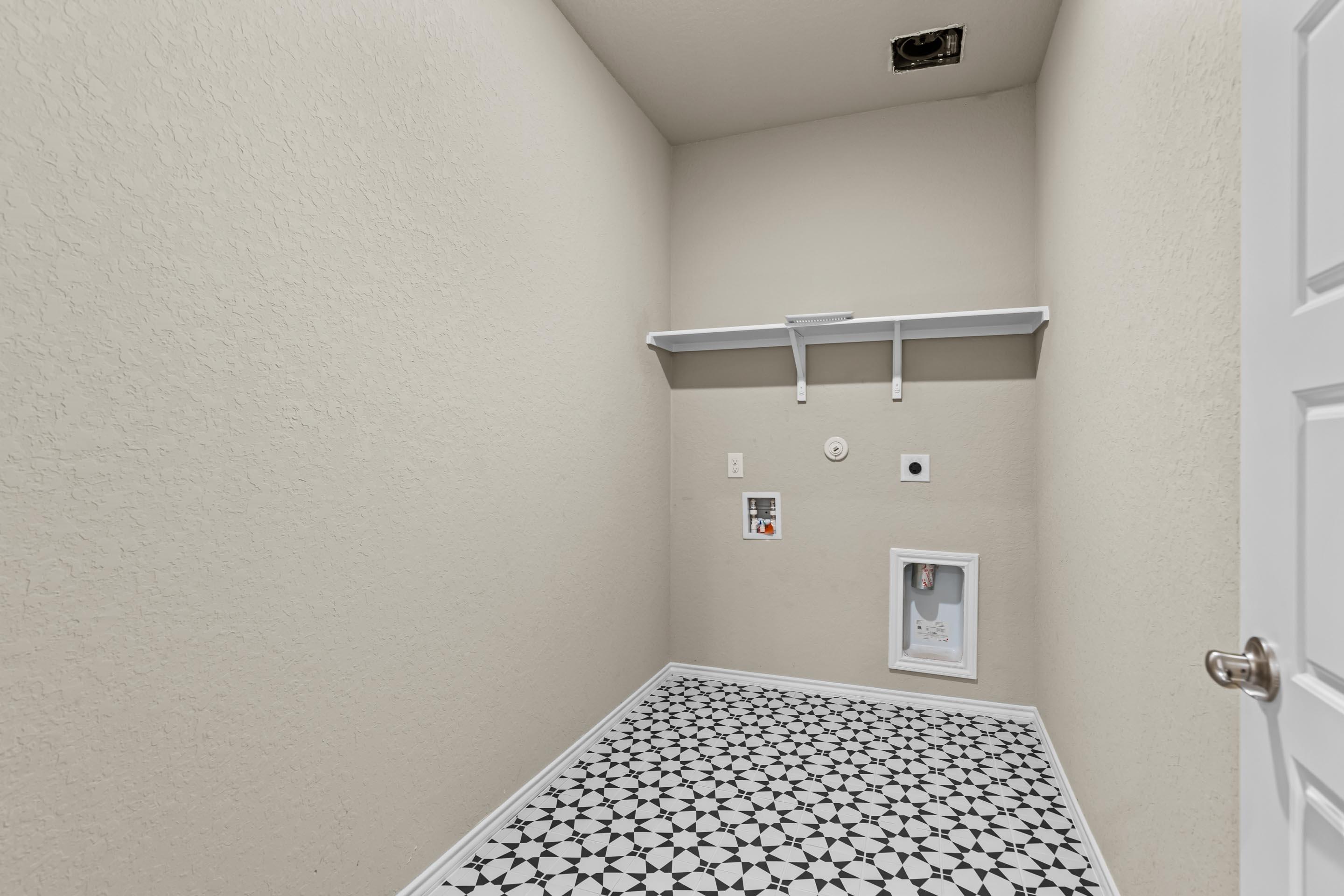 Modern laundry room with washer/dryer hookups, built-in shelves, and geometric tile floor in Davidson Homes The Douglas F, San Antonio