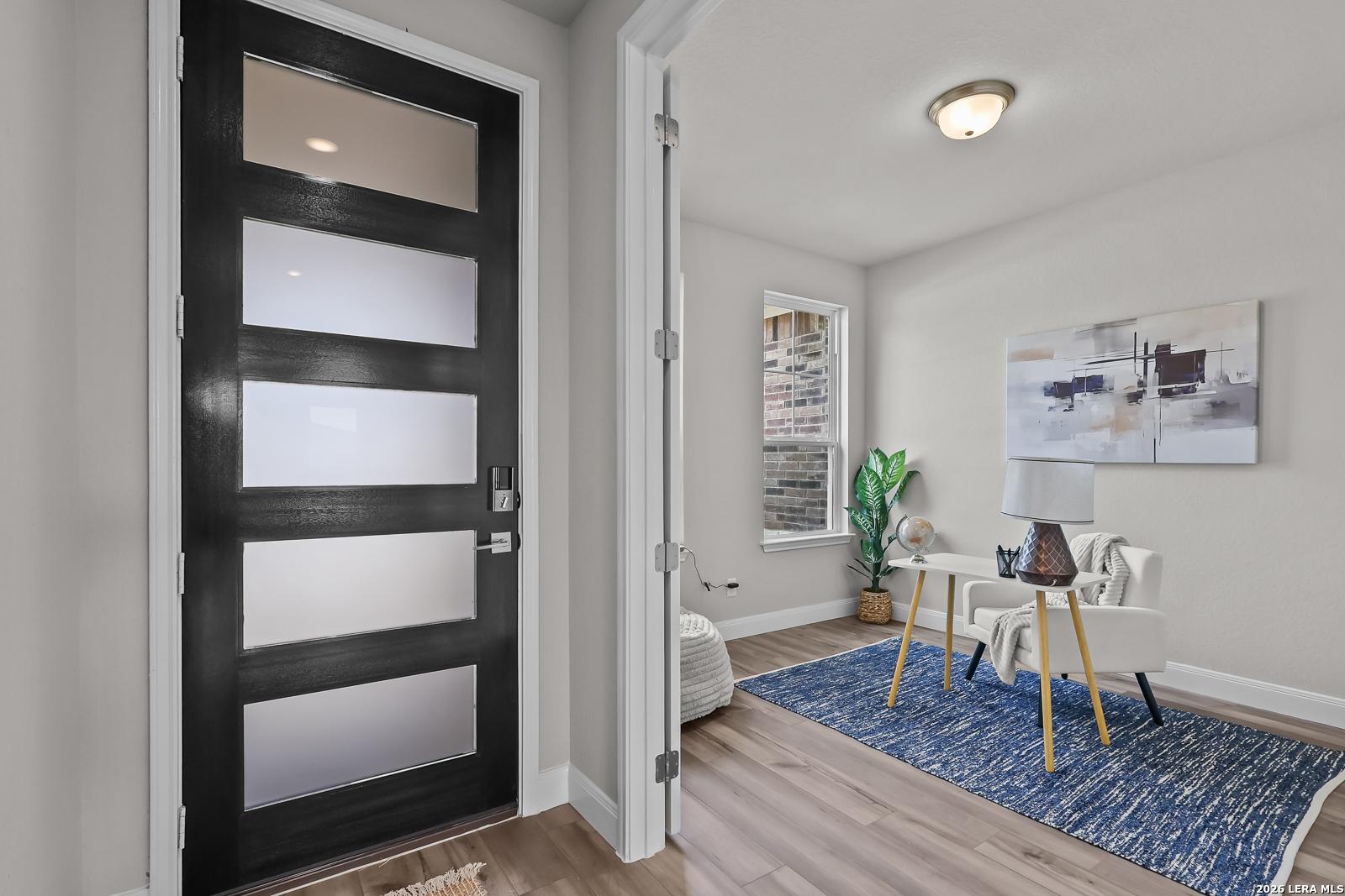 Modern entryway featuring black frosted glass door, abstract wall art, potted plant, accent chair, and blue rug on hardwood floors in Davidson Homes The Rockford G, Ladera, San Antonio