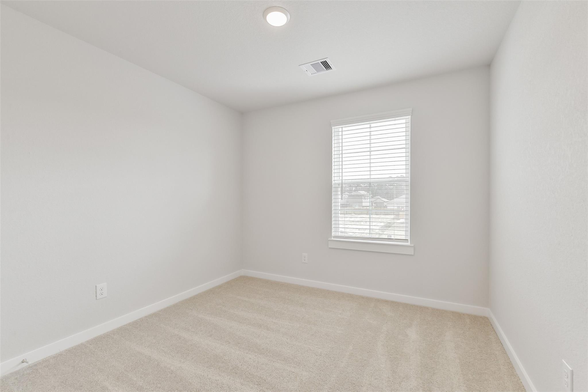 Empty secondary bedroom with beige carpet, white walls, window blinds and ceiling light in The Brazos E home, Cleveland, Texas