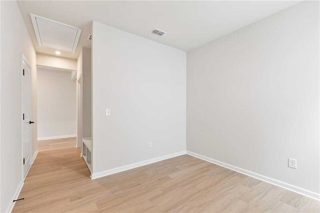 Bright secondary bedroom with light hardwood floors, neutral walls, and hallway access in Davidson Homes The Daphne C, Loganville, GA