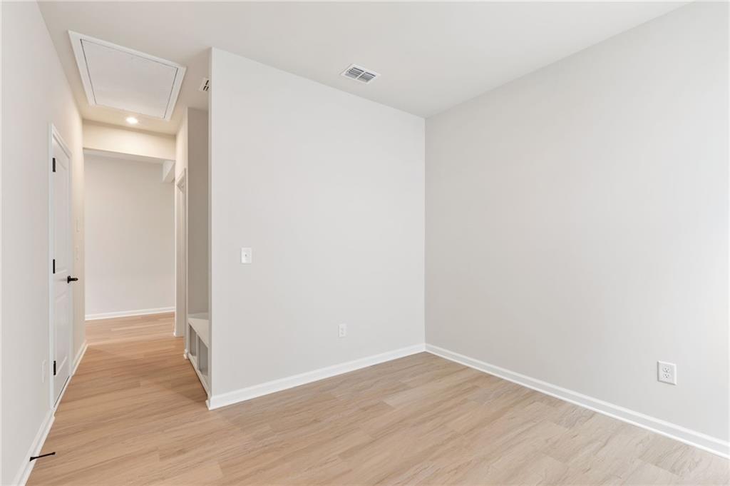 Spacious empty bedroom with light oak floors, white walls, built-in bench, and hallway in Davidson Homes The Daphne C, Loganville GA