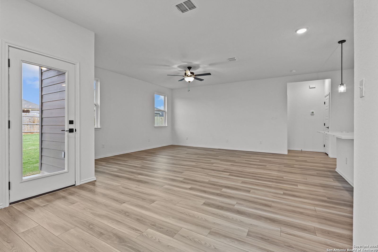 Spacious open living room with luxury vinyl plank floors, ceiling fan, and French doors to green backyard in The Daphne J home, Converse, Texas