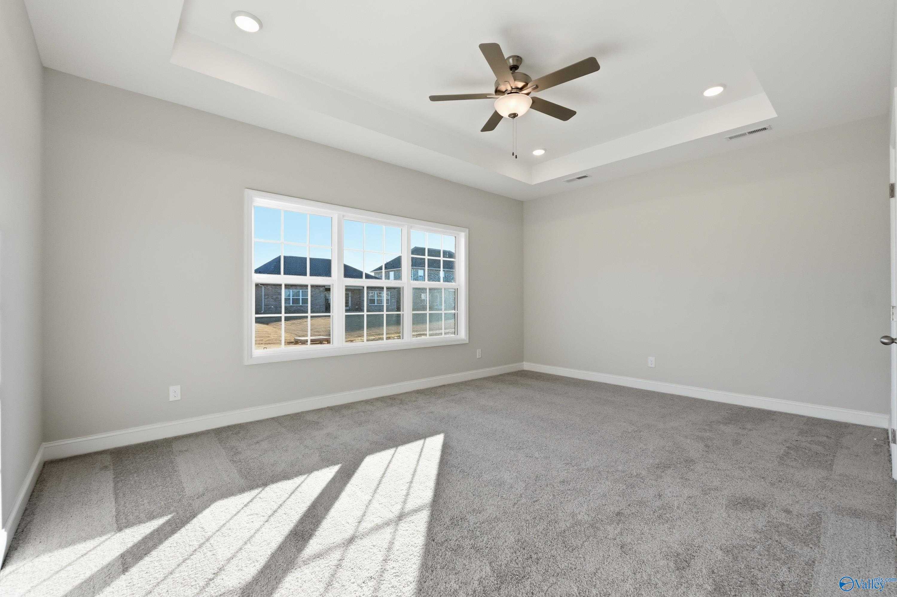 Bright bedroom with large sunny windows, ceiling fan, and gray carpet in Davidson Homes The Montgomery B, Toney, Alabama