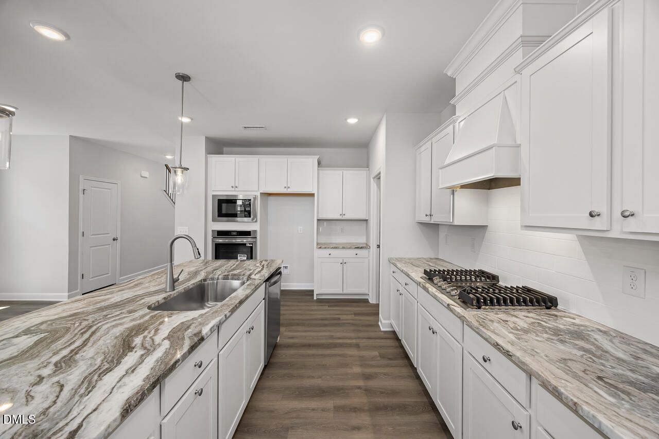 Modern kitchen with white cabinets, marble-style countertops, and gas cooktop in The Adalynn A at Gregory Village, Lillington.