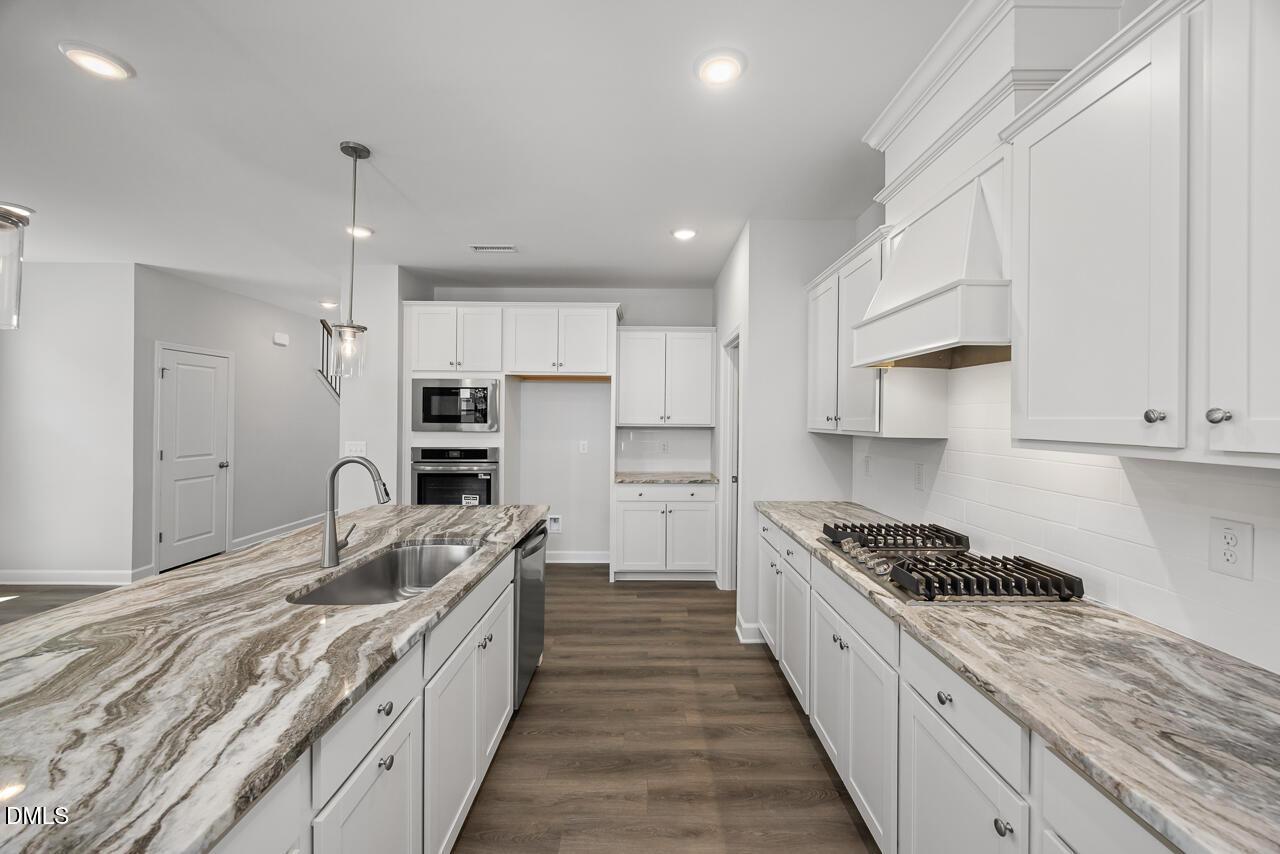 Modern kitchen with white cabinets, marble-style countertops, and gas cooktop in The Adalynn A at Gregory Village, Lillington.