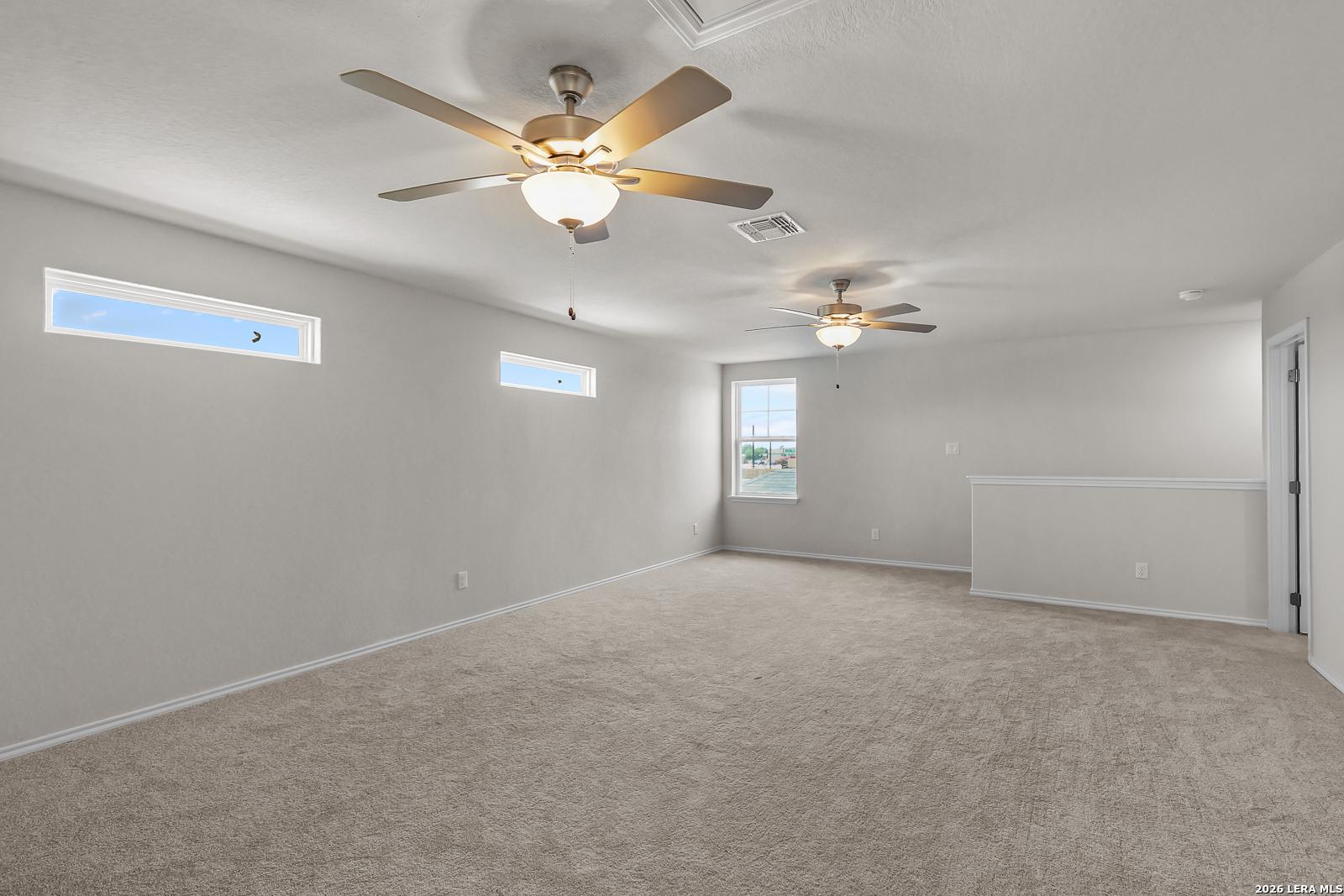 Spacious carpeted game room with ceiling fans in San Marcos F floor plan at Rayburn Valley, San Antonio, Texas.
