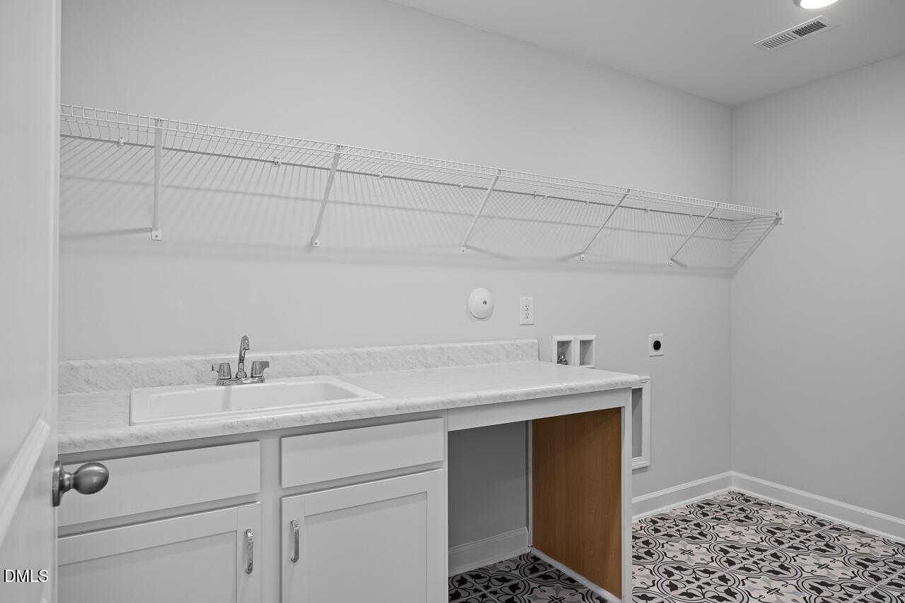 Laundry room with utility sink, white cabinetry, and patterned tile floor in The Hickory II B home, Zebulon, NC.