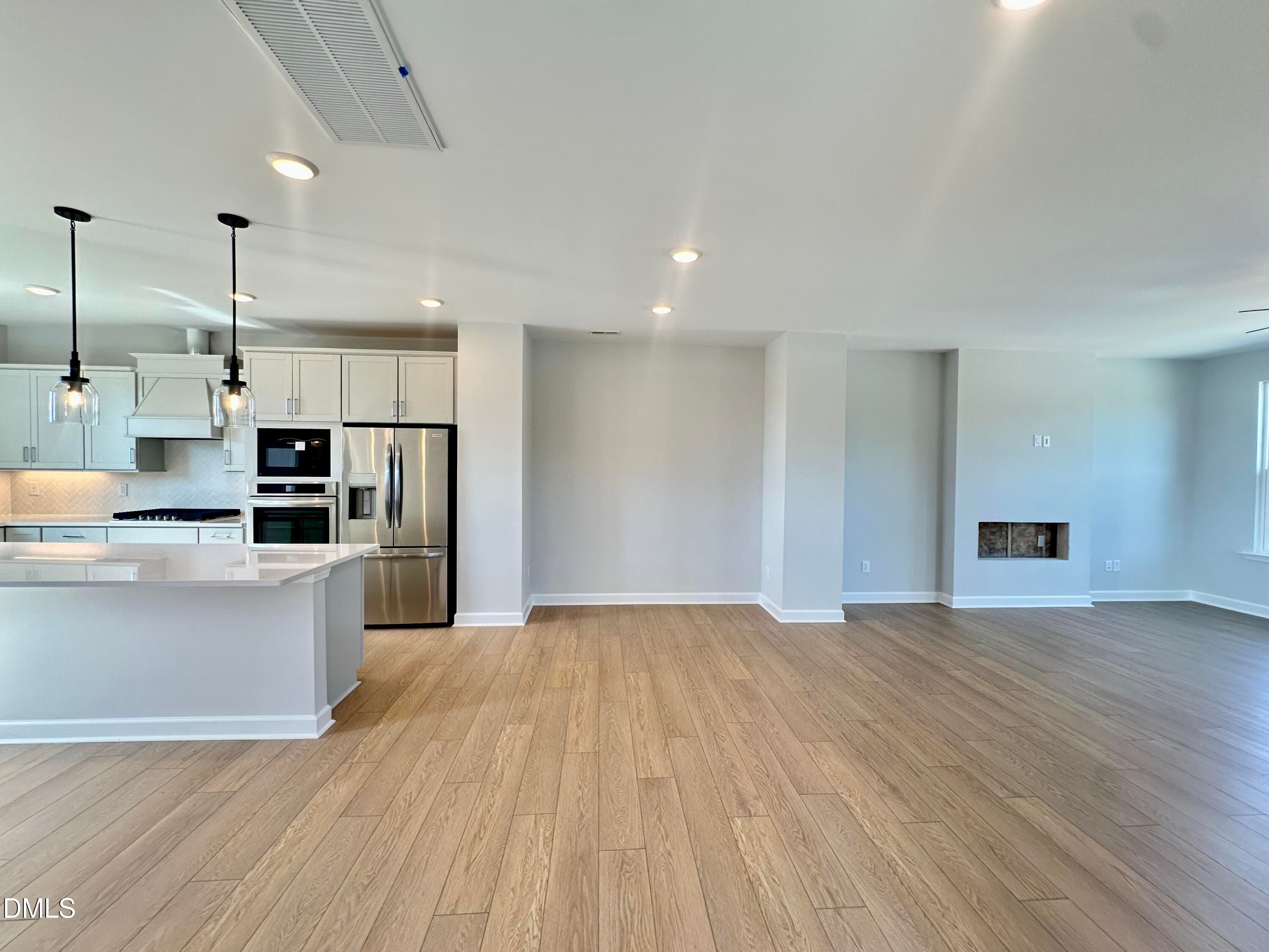 Modern open-concept kitchen with white cabinets, stainless appliances, quartz island, and living area fireplace in Davidson Homes The Avery, Knightdale NC